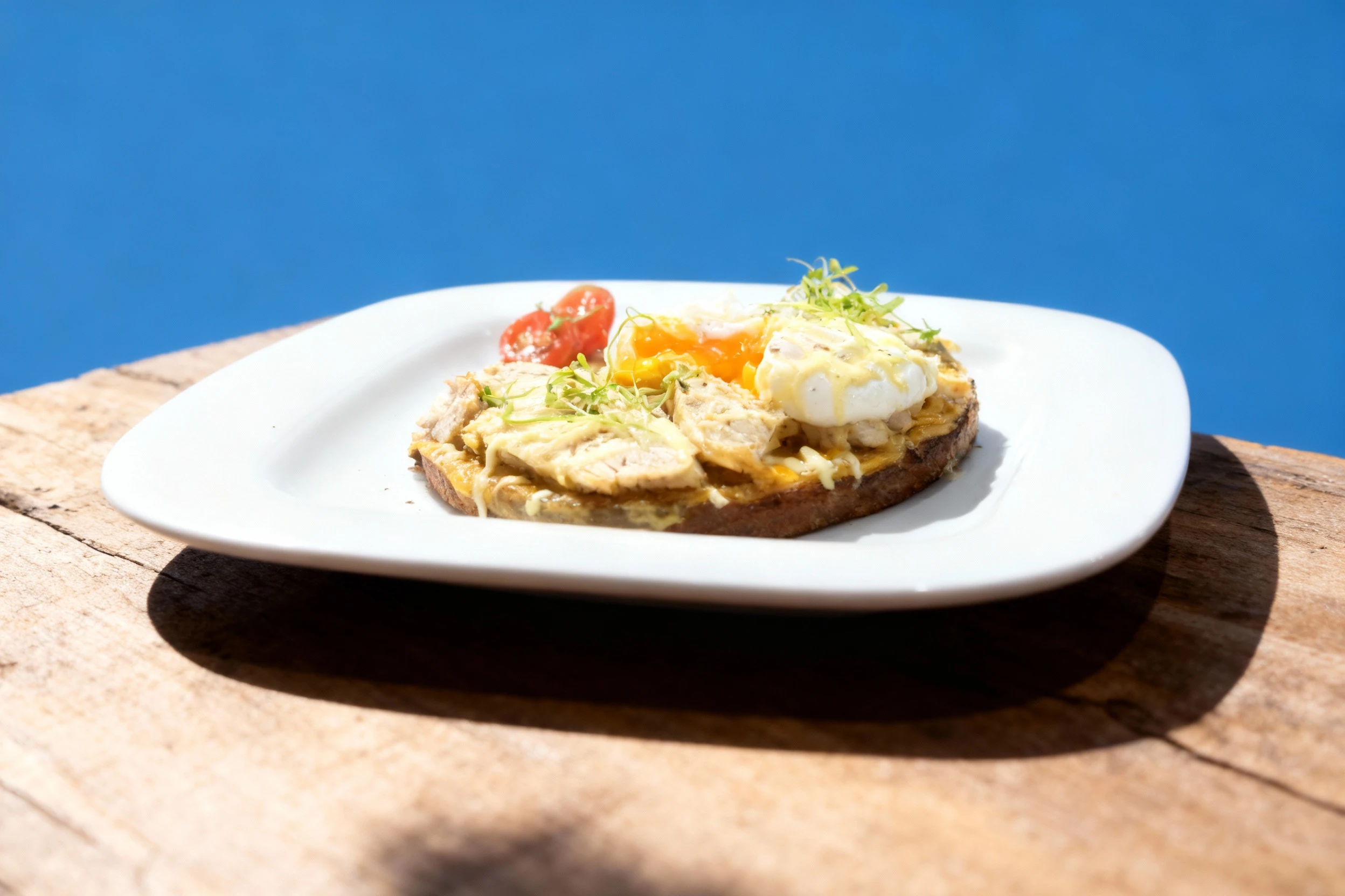 An open-faced dish, likely a brunch item, featuring a base topped with slices of white meat and a creamy sauce, finished with a poached egg with a flowing yolk