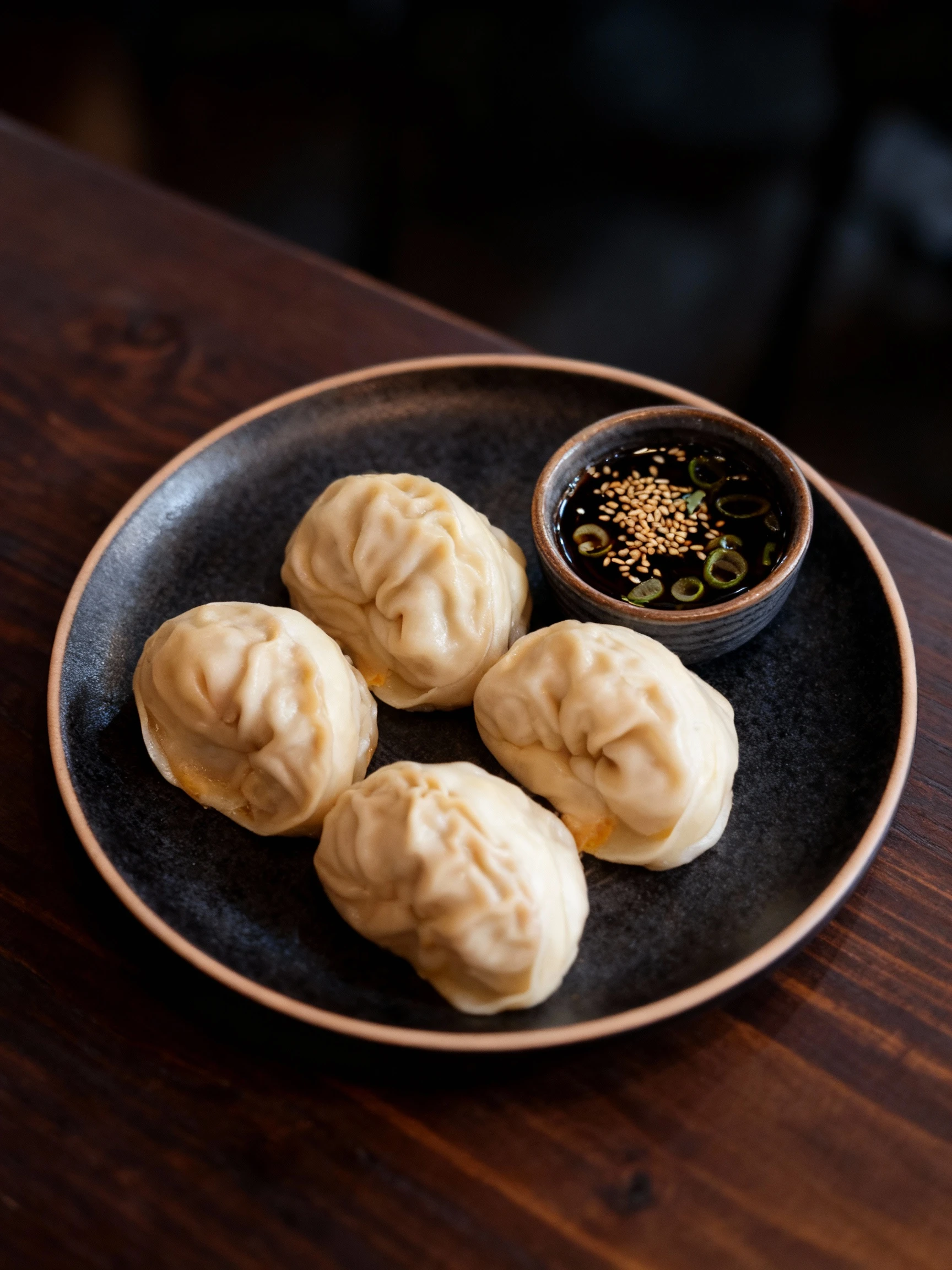 Four large steamed mandu dumplings arranged on a grey textured tray with a built-in sauce compartment.