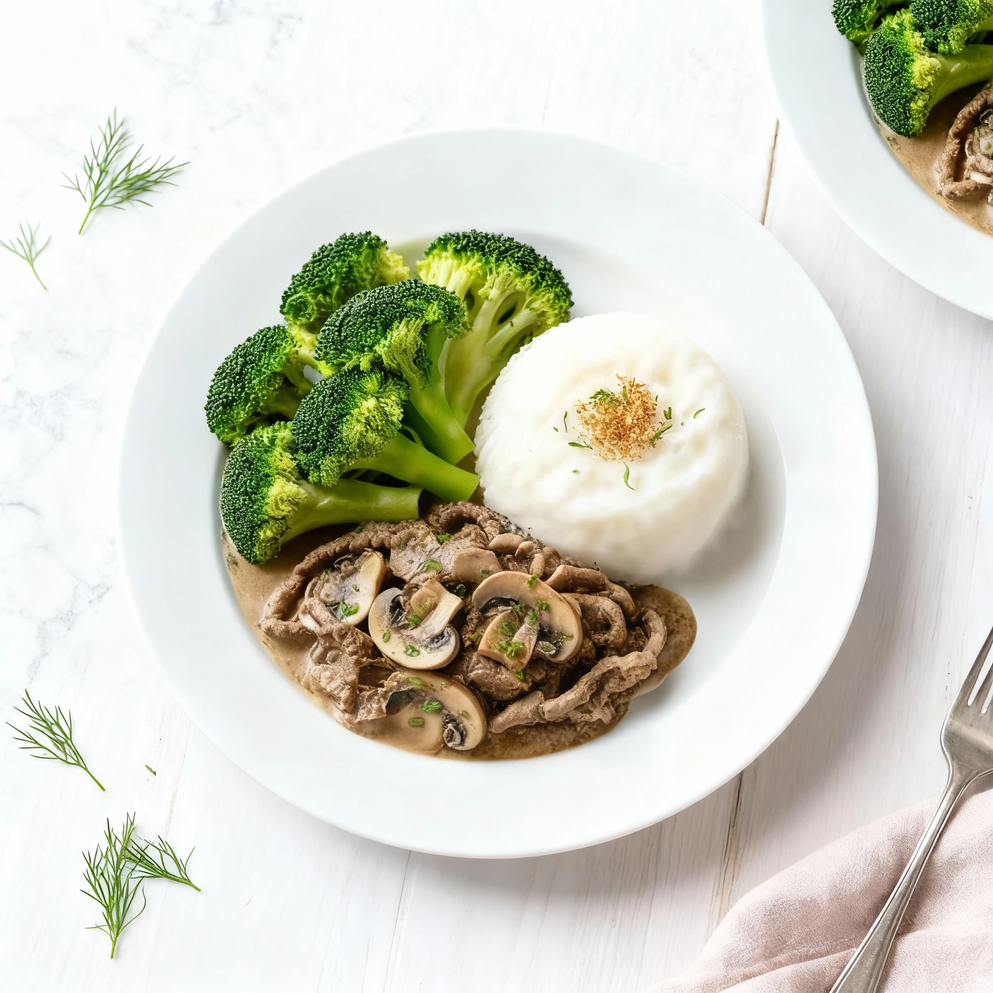 This dish features thinly sliced beef and mushrooms served in a creamy sauce, resembling beef stroganoff. It is professionally plated alongside a dome of mashed