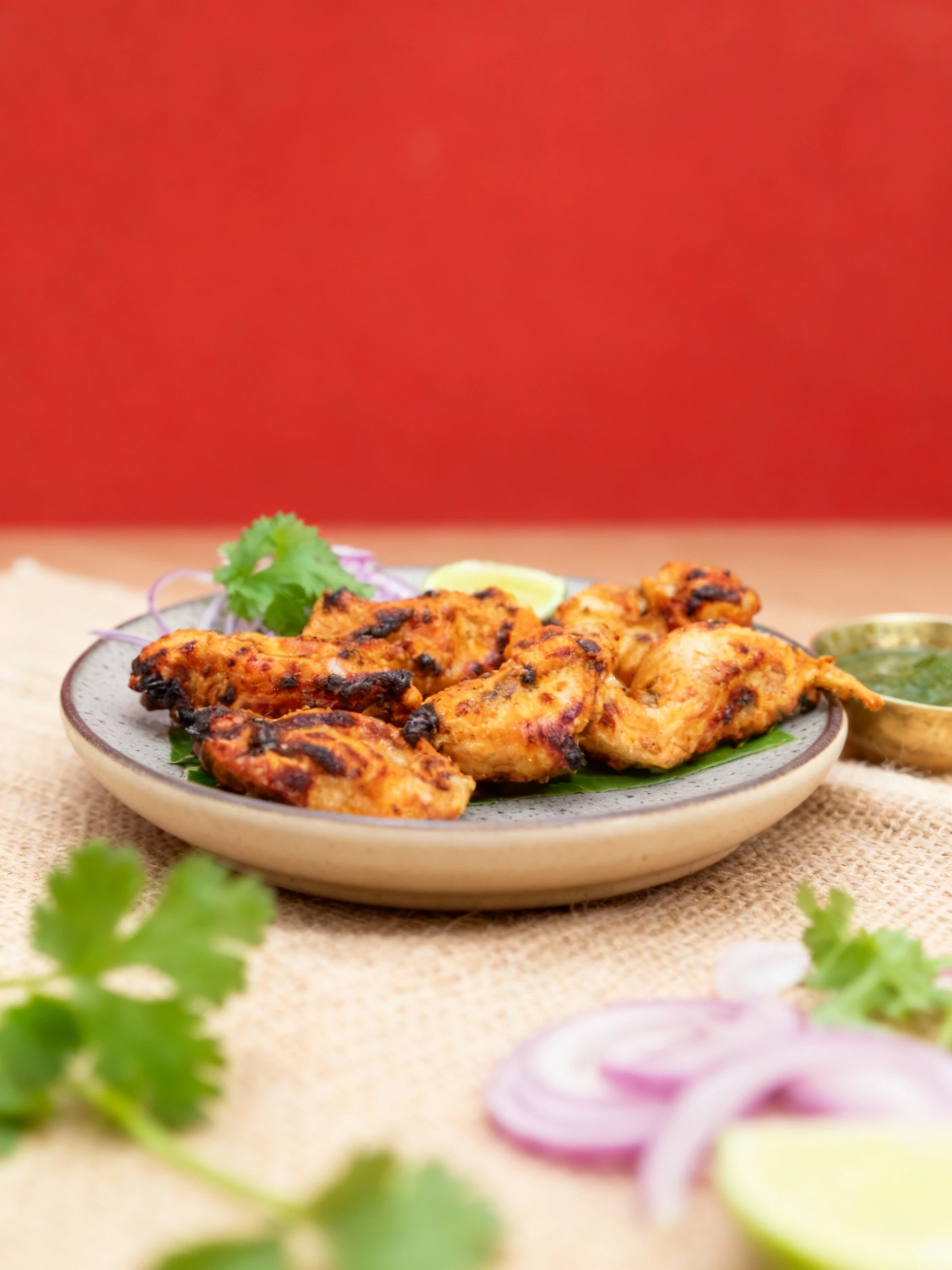 Grilled and charred pieces of marinated chicken, likely chicken tikka, are served on a plate with sliced red onions, a cilantro garnish, and a lime wedge, accom