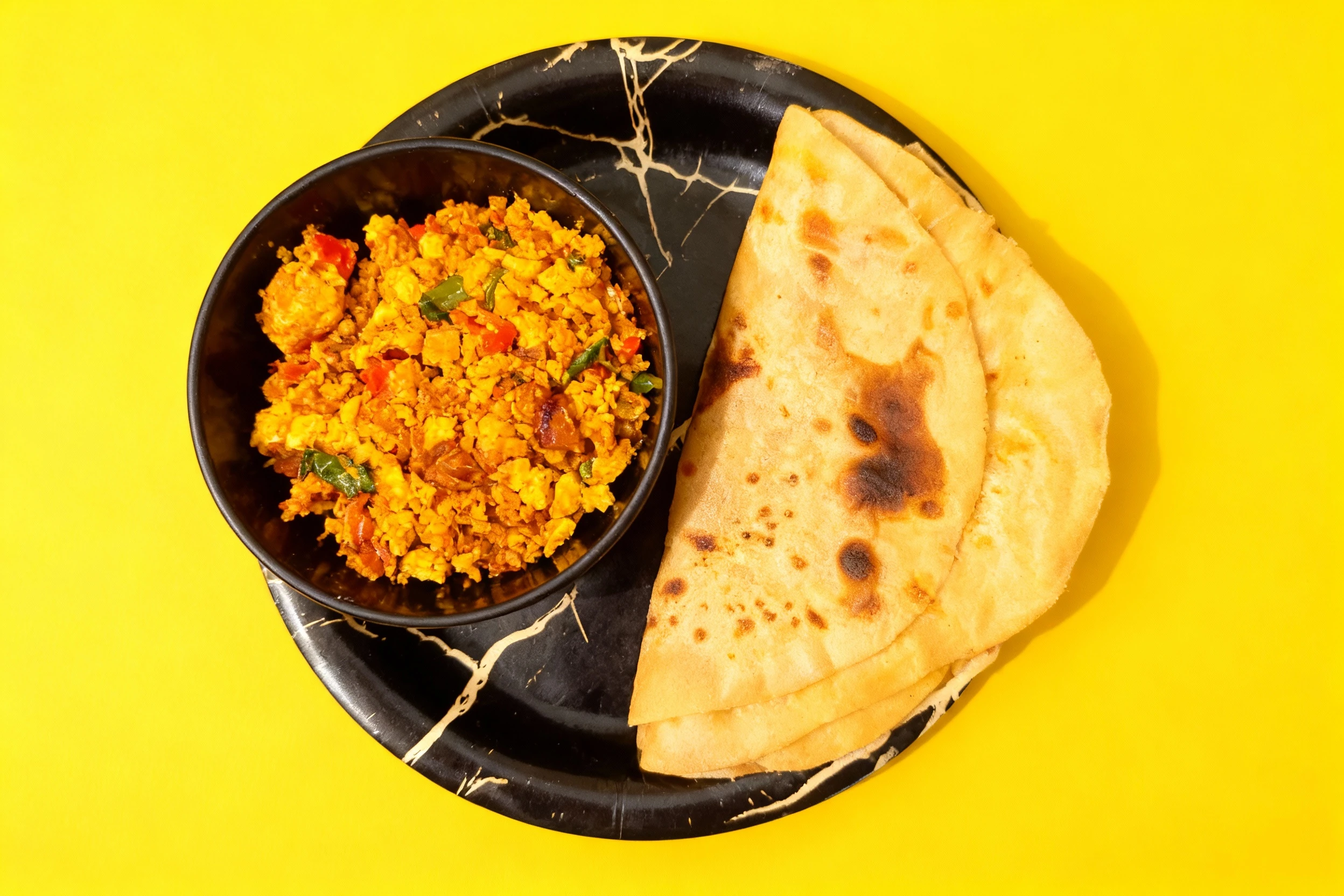 A folded, toasted flatbread served alongside a bowl of spiced paneer bhurji mixed with herbs and vegetables.
