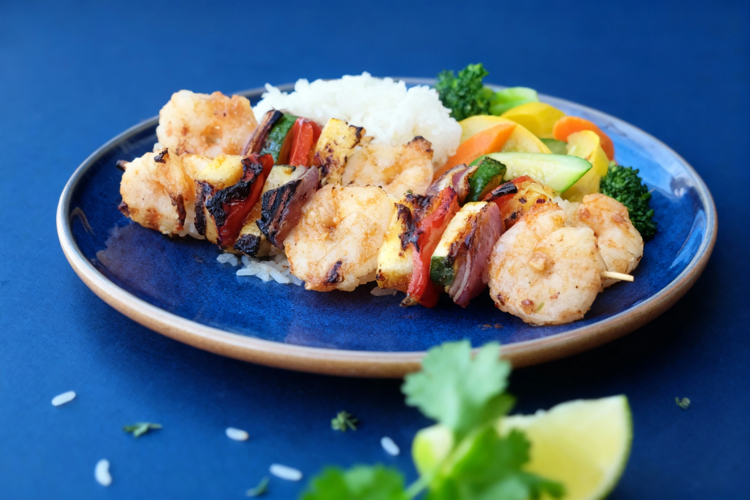 Grilled shrimp skewers with charred pineapple, red onion, zucchini, and bell peppers served over white rice with a side of steamed broccoli and squash.