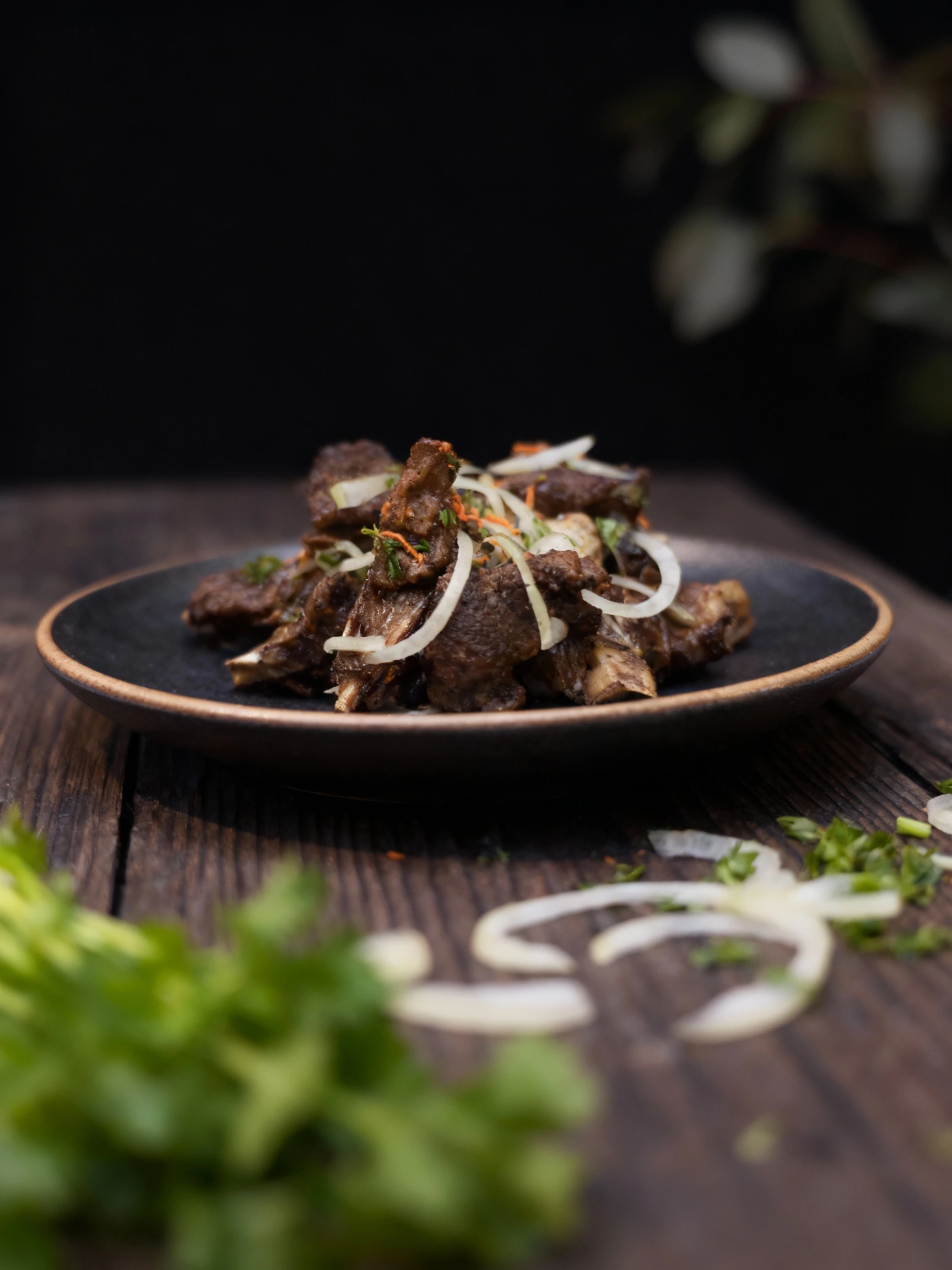 A close-up view of dark, well-cooked pieces of meat, possibly short ribs or shashlik, piled high on a white plate and heavily garnished with raw white onion sli