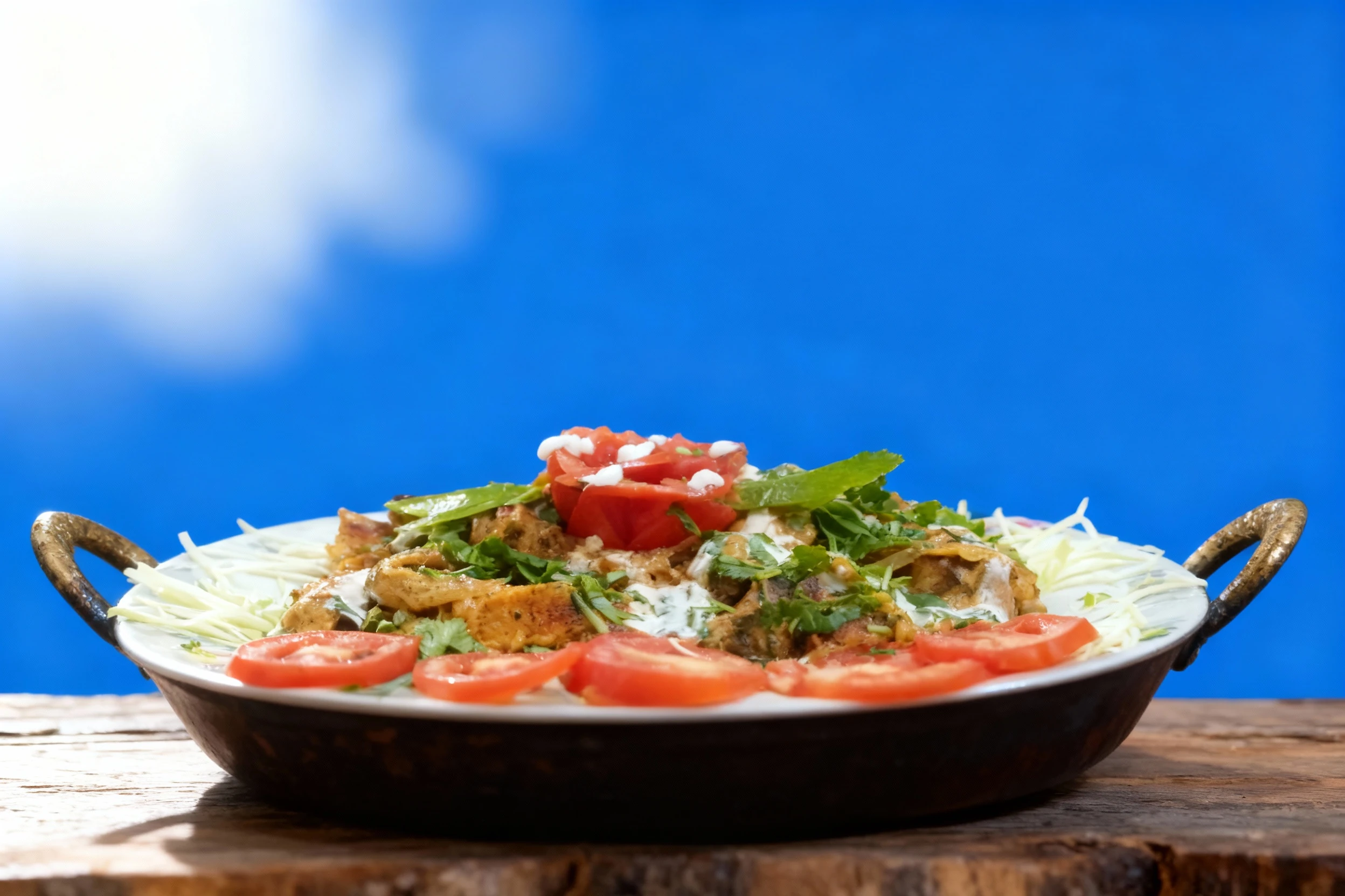 Grilled chicken pieces coated in a creamy sauce and topped with fresh cilantro, served with sliced tomatoes and shredded cabbage garnish.