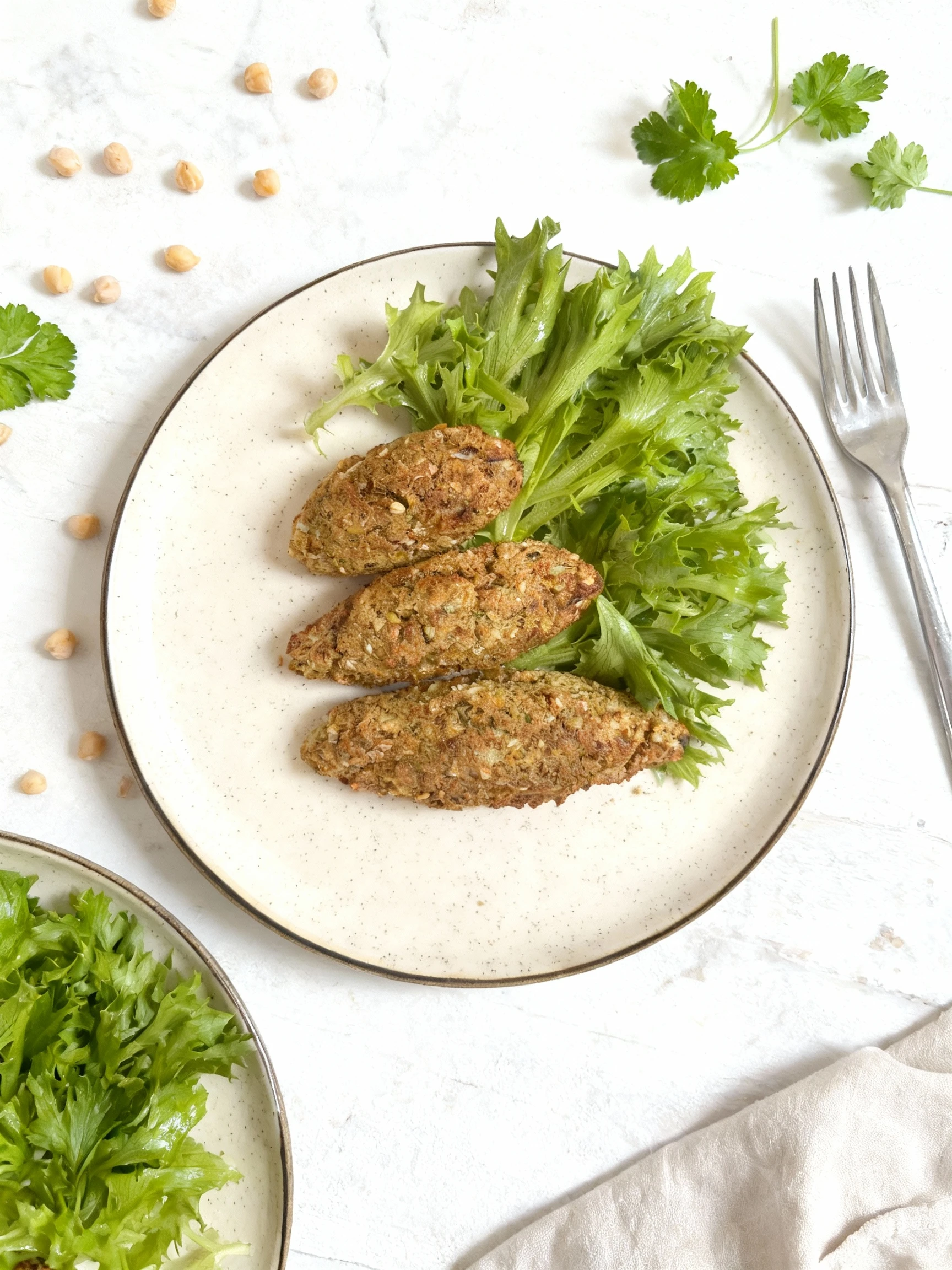 Three herb-flecked falafel or vegetable croquettes served on a speckled ceramic plate alongside a bunch of fresh green leaf lettuce.