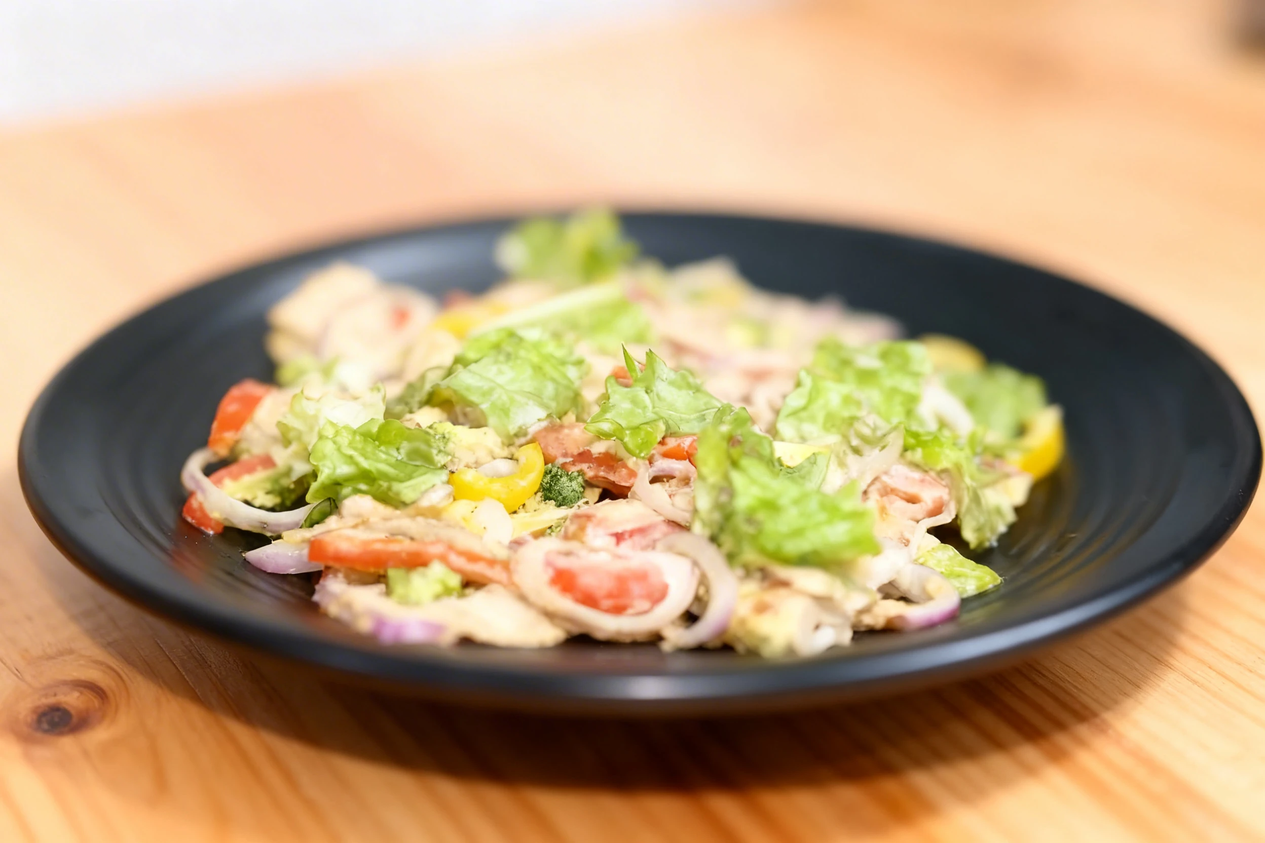 Mixed garden salad featuring chopped lettuce, sliced red onions, yellow bell peppers, and fresh tomatoes tossed with a creamy dressing.