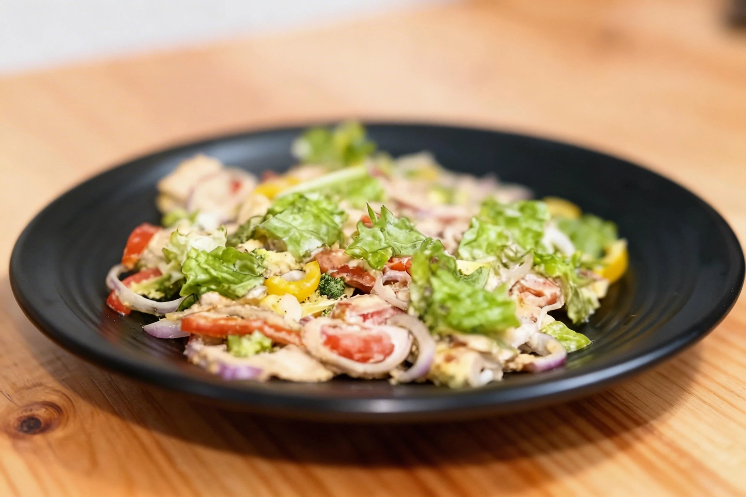 Mixed garden salad featuring chopped lettuce, sliced red onions, yellow bell peppers, and fresh tomatoes tossed with a creamy dressing.