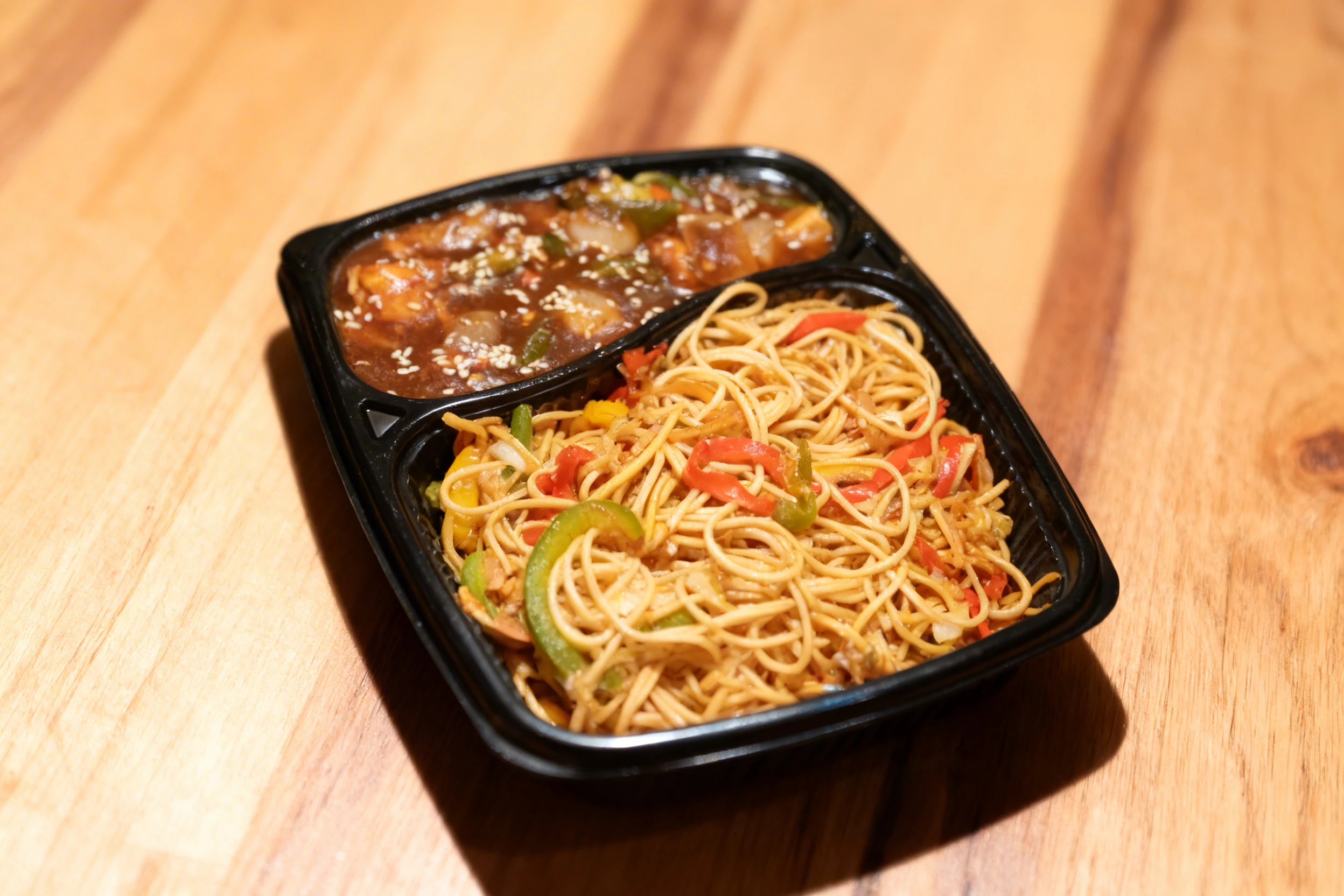 A takeout platter featuring vegetable stir-fry noodles with sliced peppers and a side of chili paneer gravy garnished with sesame seeds.
