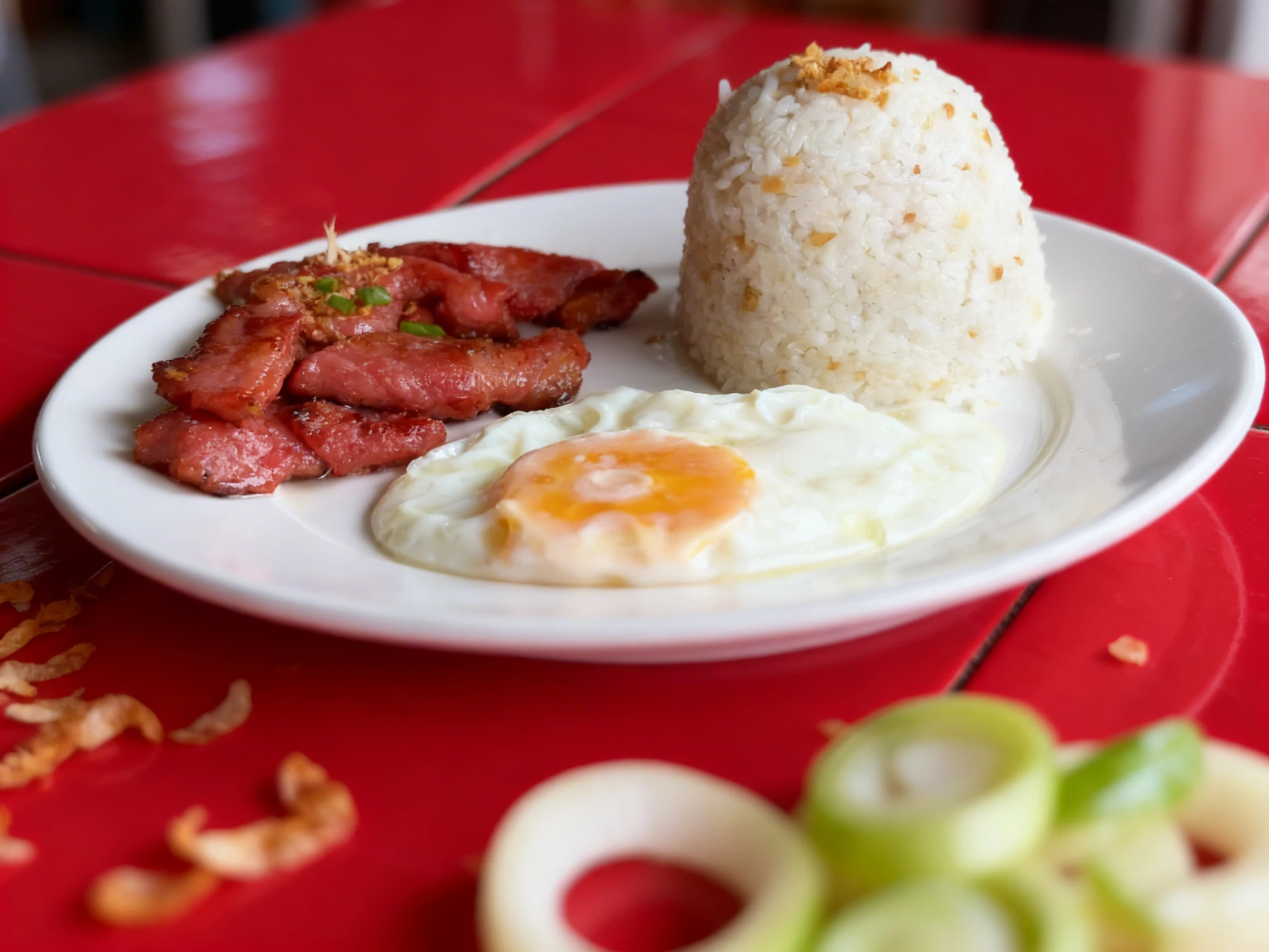 A traditional Filipino Tapsilog breakfast featuring cured beef slices topped with fried garlic and scallions, served with a sunny-side-up egg and a mound of gar