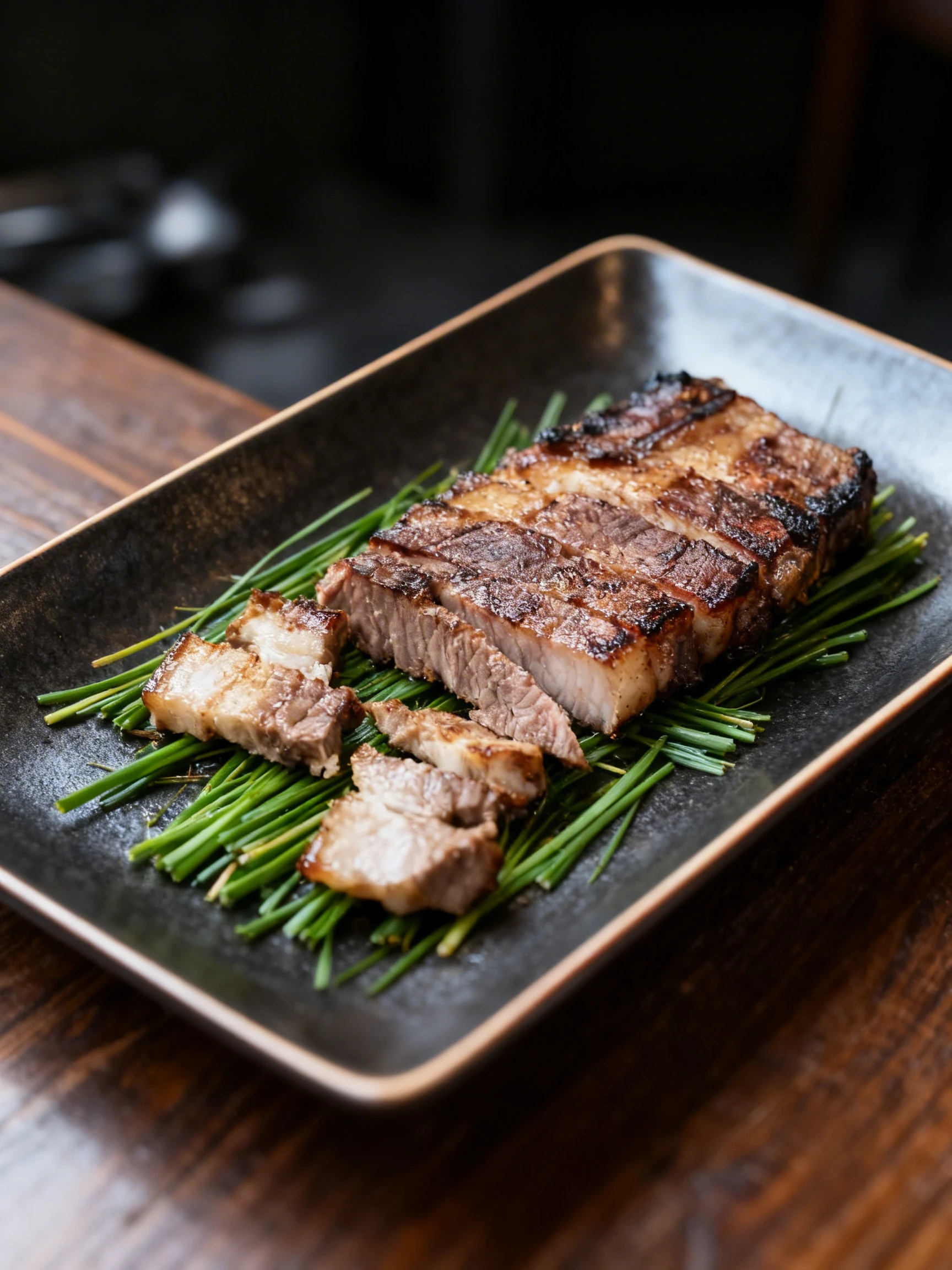 Grilled Korean black pork belly and neck steaks, including seared whole cuts being sliced and bite-sized pieces served over a bed of green chives.