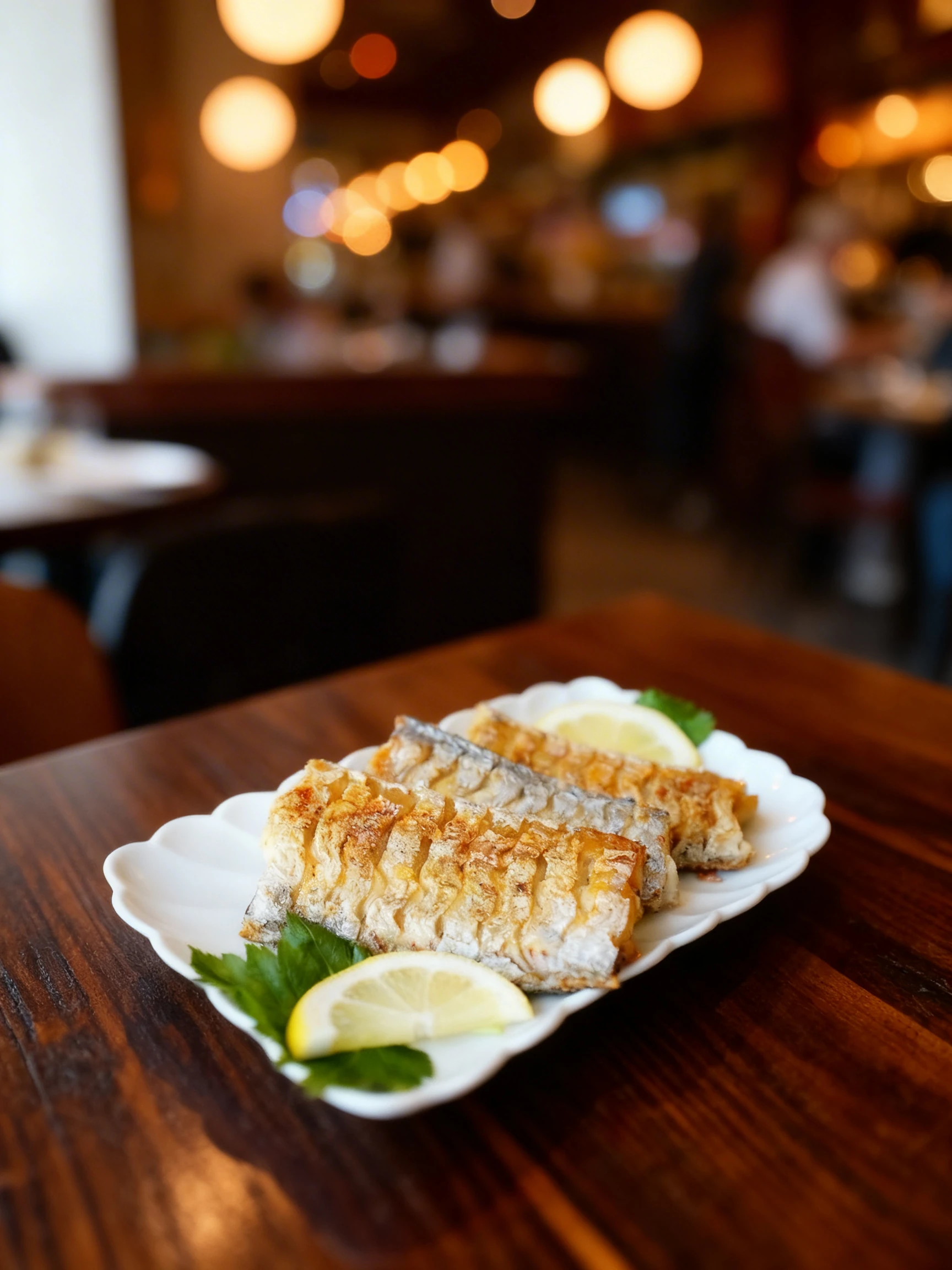 Pan-fried hairtail fish fillets served on a white scalloped plate with fresh lemon slices and green herbs.