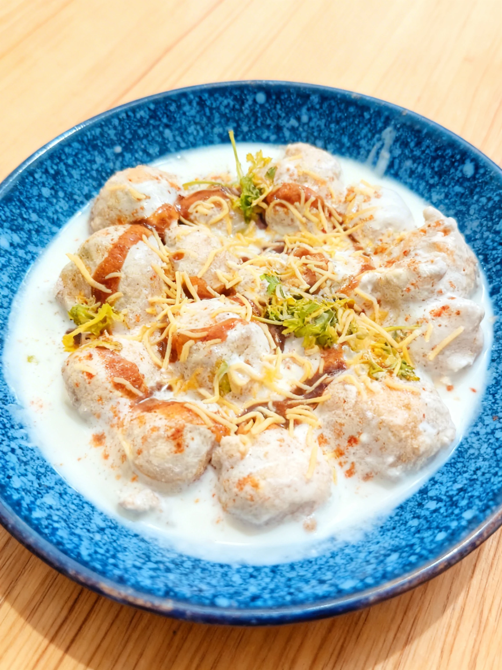 Dahi Vada featuring deep-fried lentil fritters soaked in thick yogurt, topped with sweet tamarind chutney, spicy green chutney, red chili powder, and crunchy se