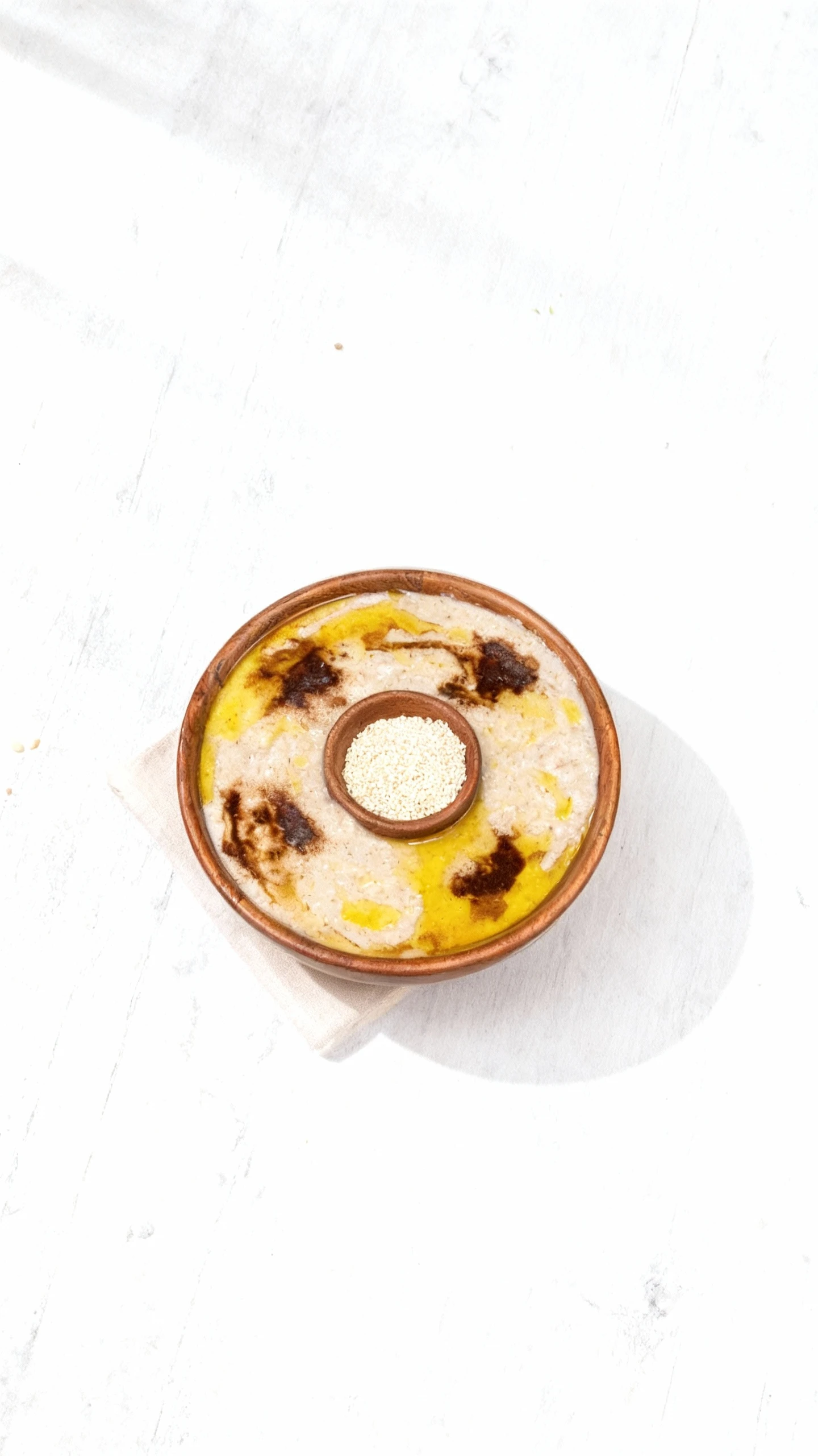 A bowl of creamy, light-colored savory porridge, likely Jareesh or Harees, topped with melted golden clarified butter and dark seasoning streaks. A small wooden