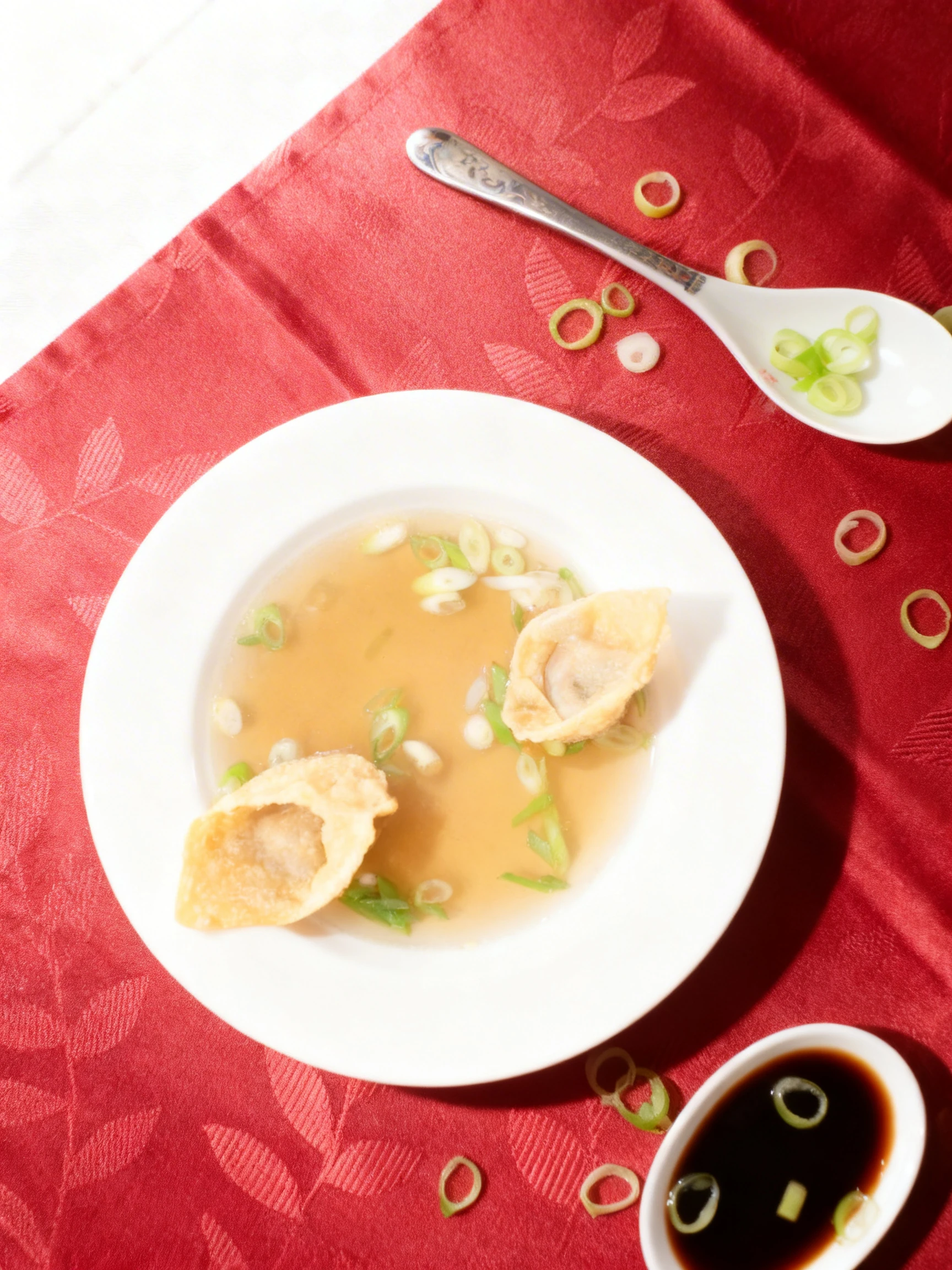 Clear broth soup served with two fried wontons and sliced green onions in a white bowl.