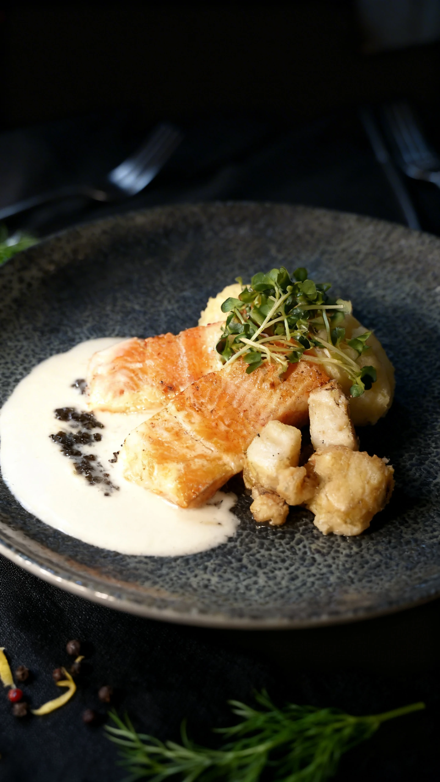 Pan-seared salmon fillet served with mashed potatoes, creamy white sauce, black caviar, and garnished with fresh microgreens.