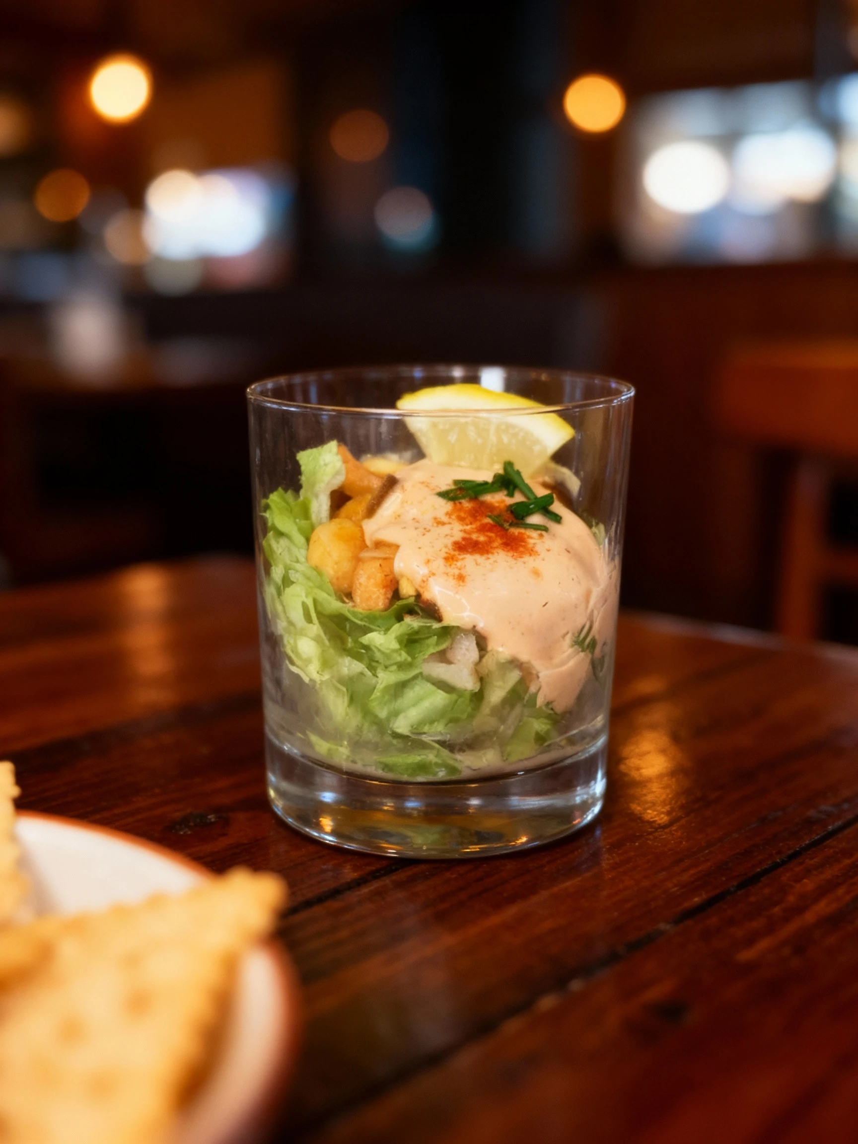 This is a layered seafood cocktail served in a glass, consisting of shredded lettuce and chunks of seafood, topped with a creamy cocktail sauce, fresh chives, p