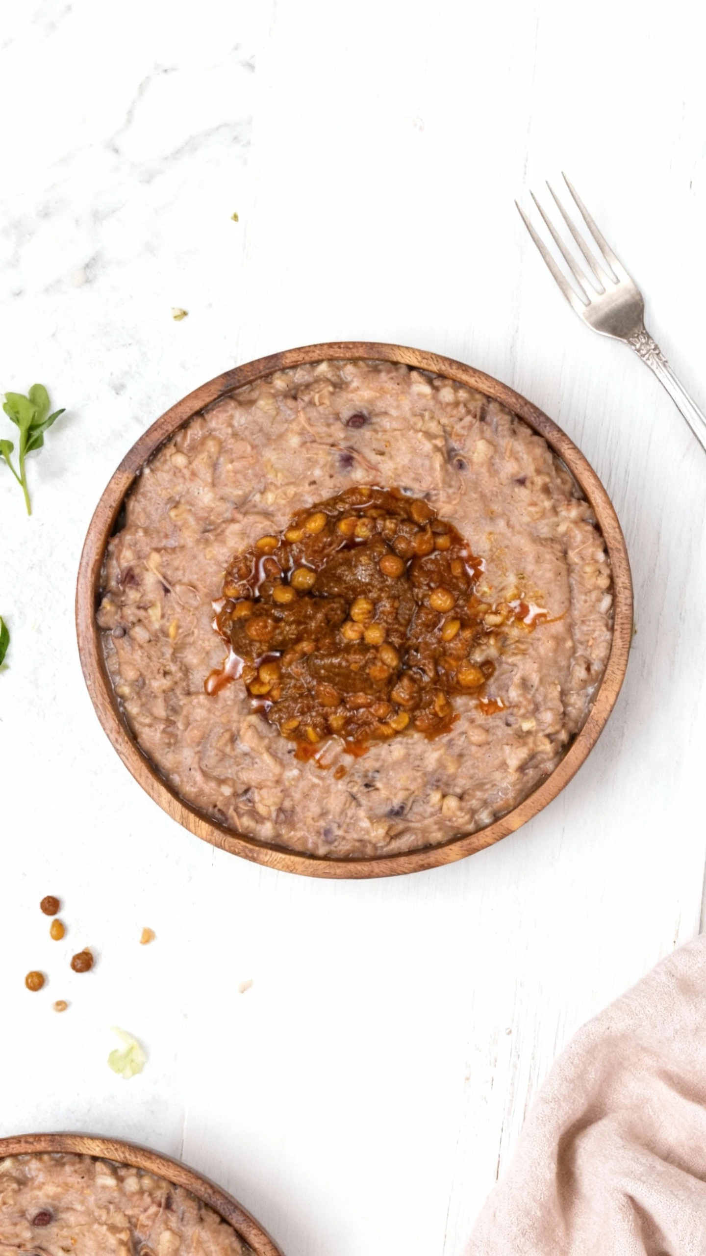 A bowl of thick, savory mash, likely a lentil or grain-based porridge (such as Haleem), centered with a rich, dark chili oil sauce containing whole split lentil