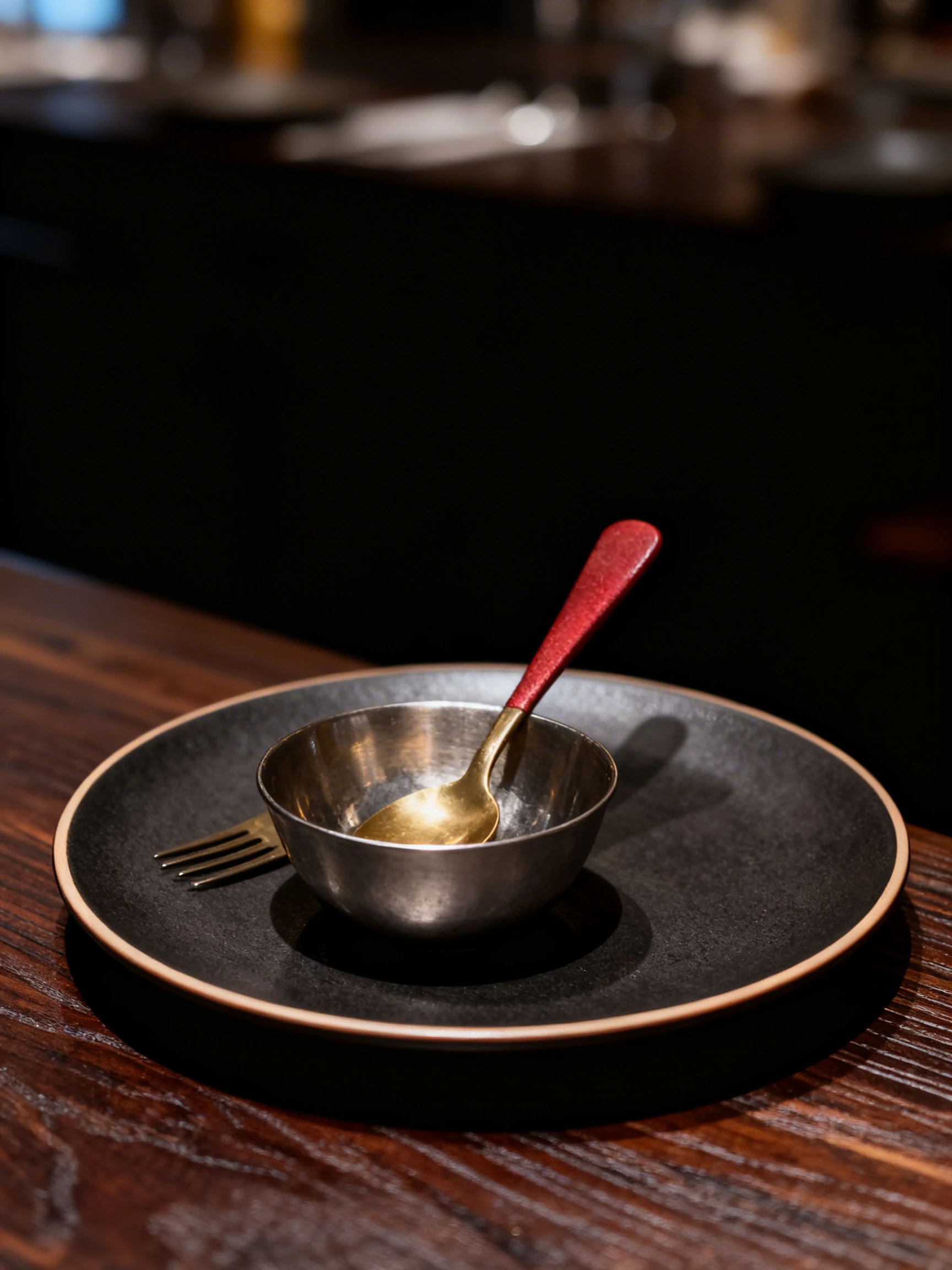 Empty small metal bowl with a gold-colored spoon inside and a matching fork resting on a woven placemat.