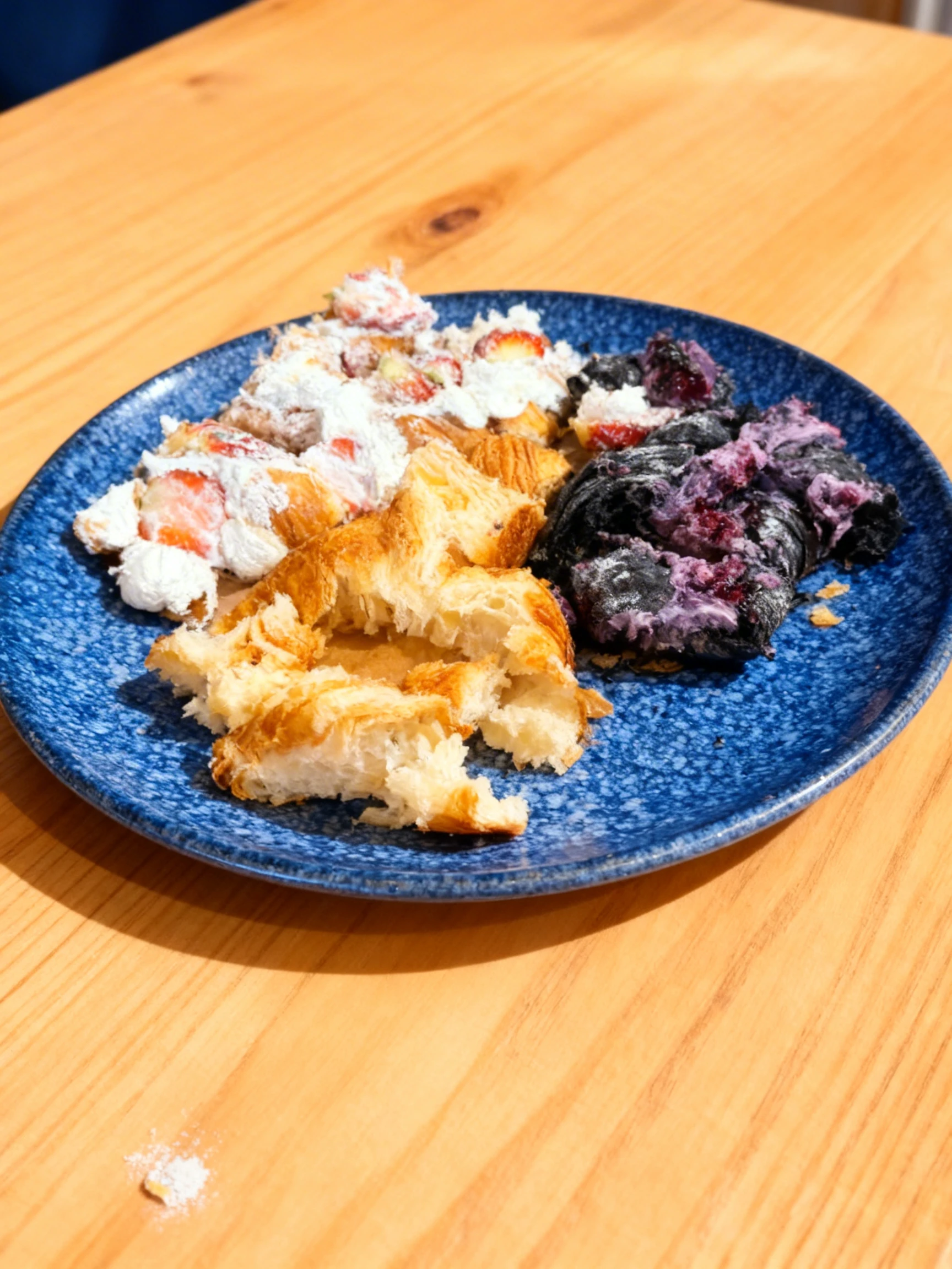 Assorted torn pastries including a golden butter croissant, a strawberry cream croissant, and a dark charcoal pastry with purple berry filling.