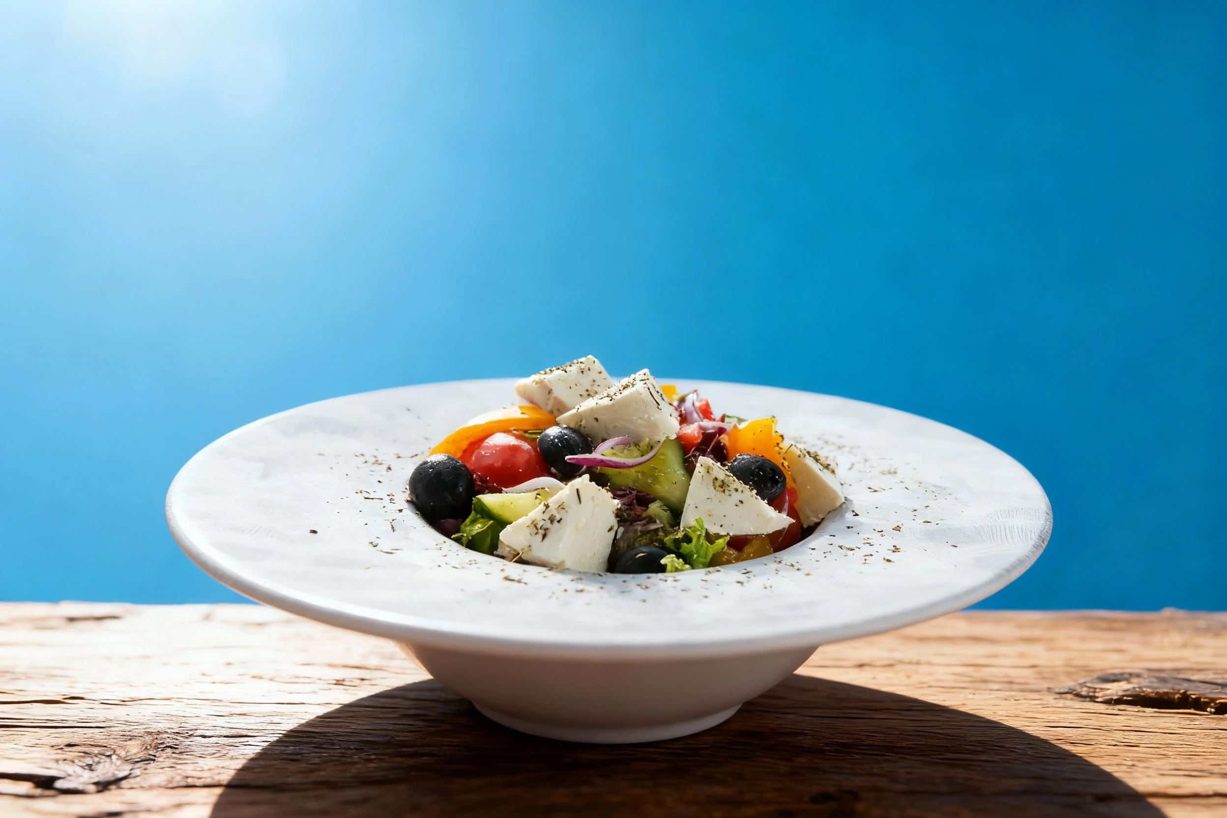 Greek salad featuring cubes of feta cheese, black olives, sliced cucumbers, tomatoes, bell peppers, and red onions seasoned with dried herbs.