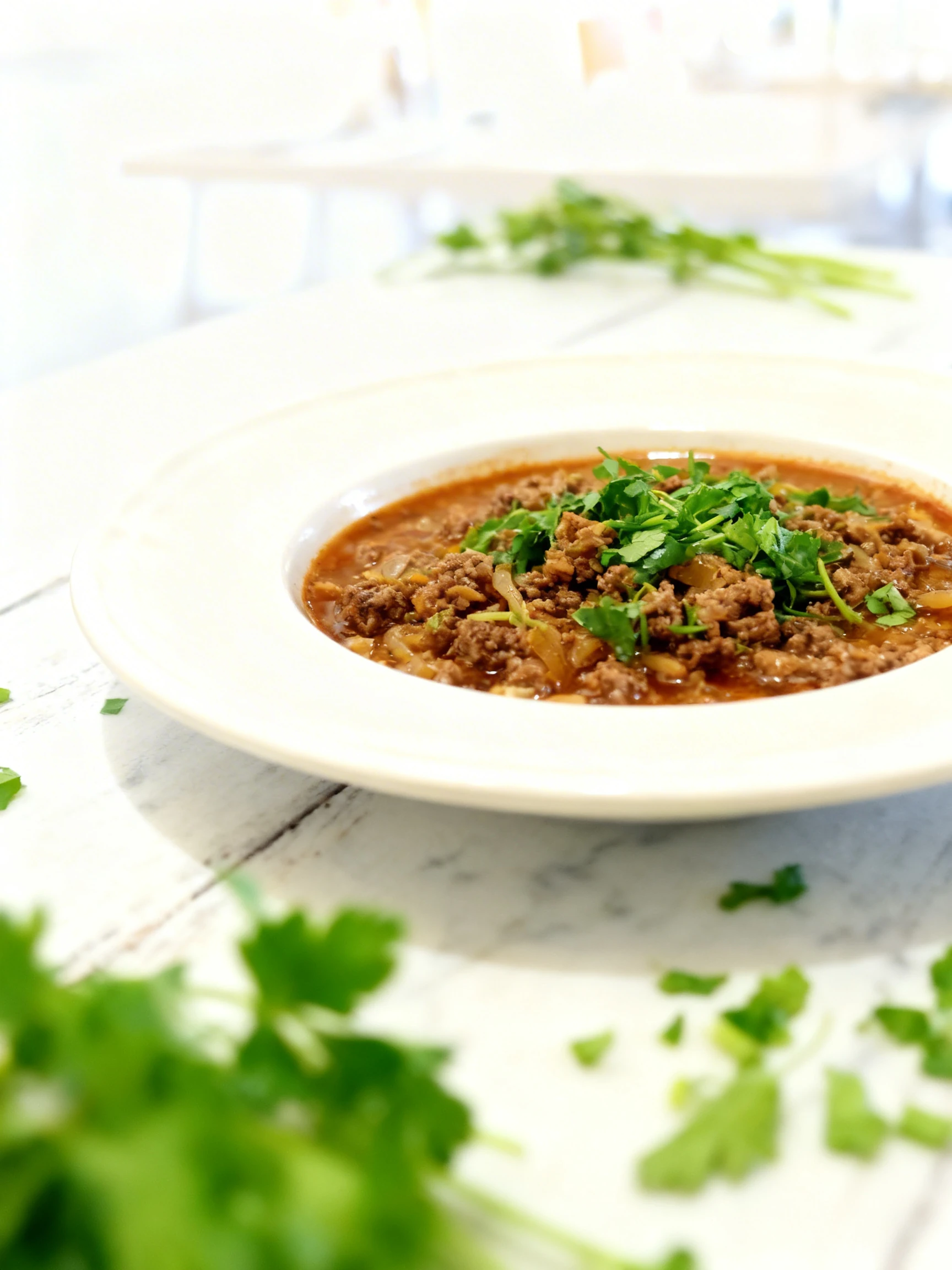 A hearty meat stew or Bolognese sauce featuring browned ground beef and sauteed onions topped with a generous portion of fresh chopped parsley.