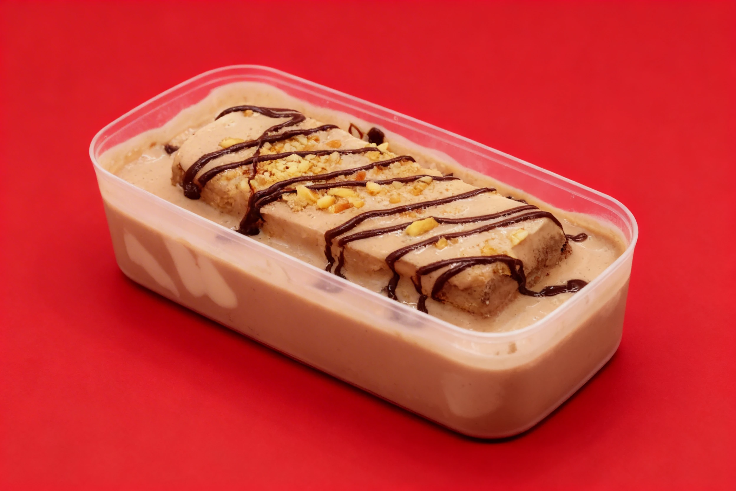 Chocolate-drizzled cake bar topped with crushed nuts, served in a creamy light brown sauce.