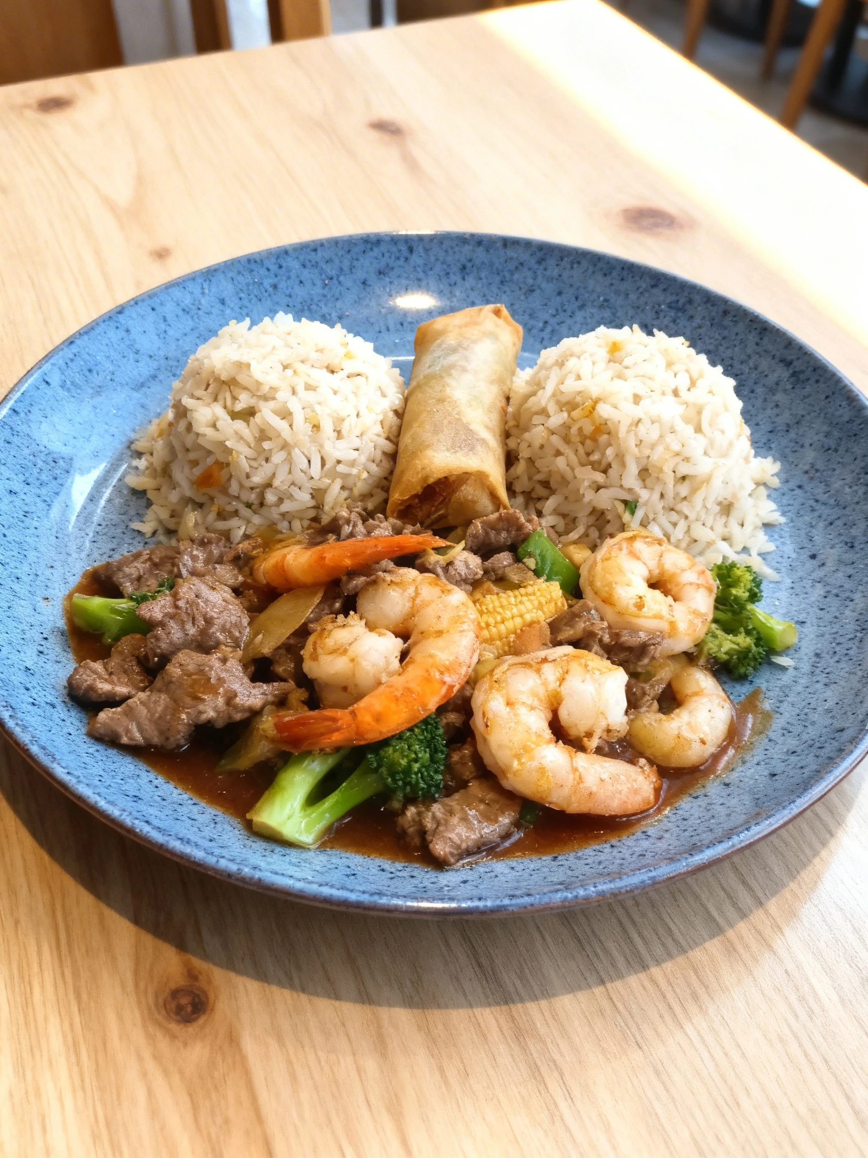 A stir-fry featuring sliced beef, large shrimp, broccoli florets, and baby corn in a dark sauce, served with two scoops of fried rice and a vegetable spring rol