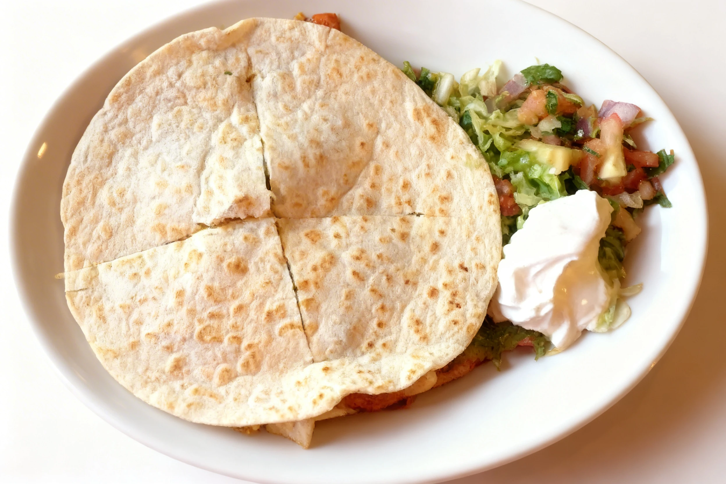 A four-cut grilled flour tortilla quesadilla served with a side of pico de gallo, shredded lettuce, and a dollop of sour cream.