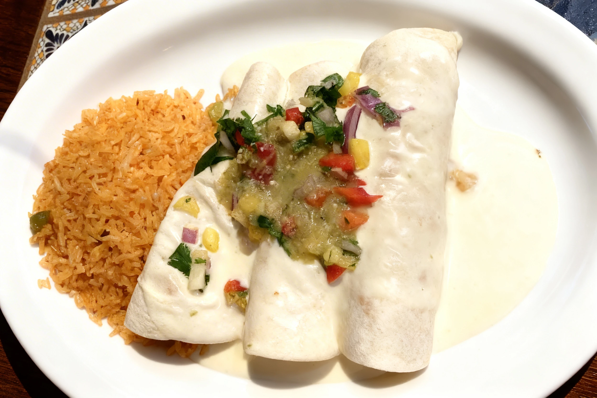 Three flour tortillas filled and smothered in white queso sauce, topped with fresh pico de gallo and salsa verde, served alongside a portion of Mexican seasoned