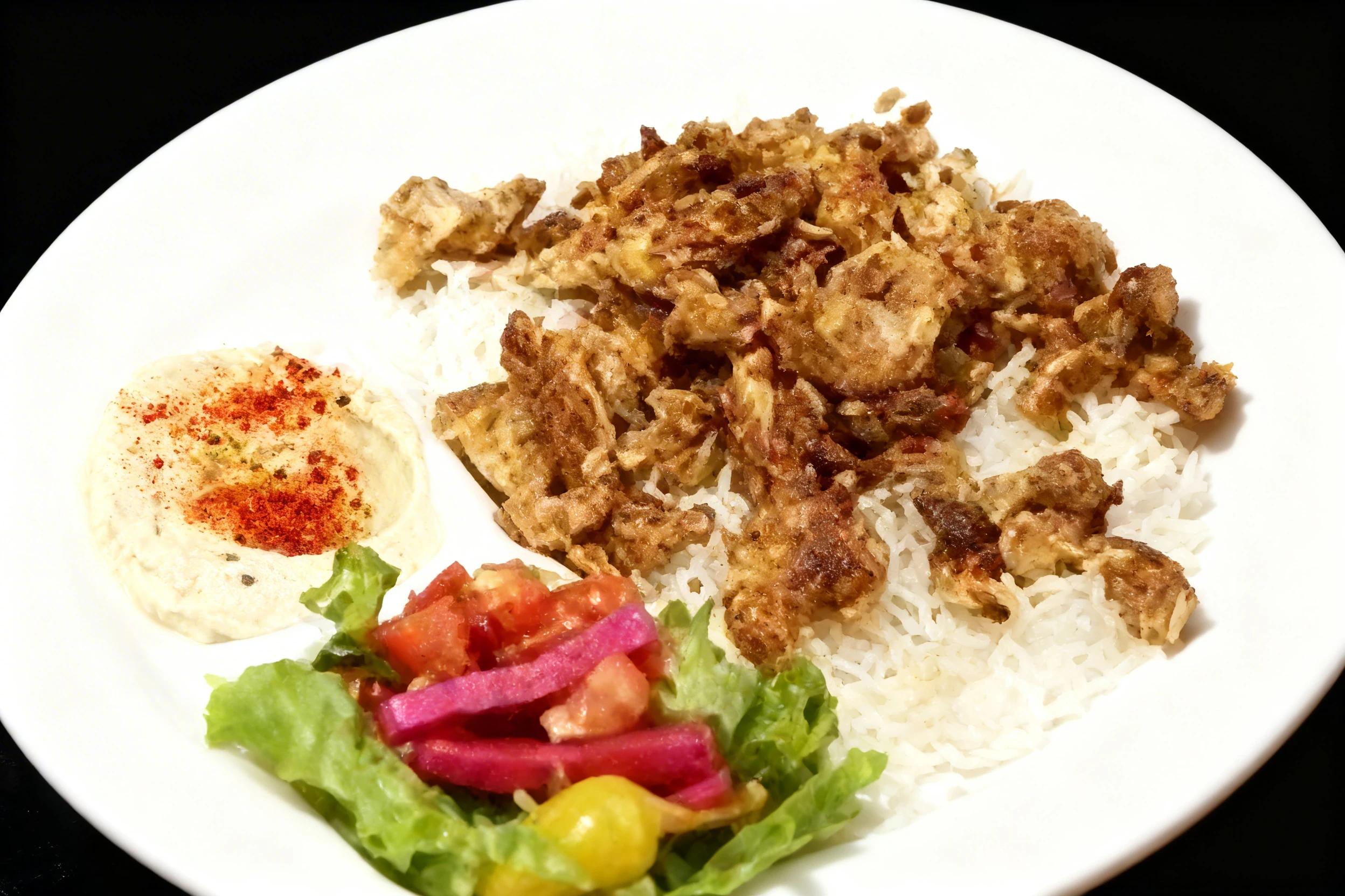 Chicken shawarma platter served over white rice with a side of hummus topped with chili flakes and a fresh salad containing lettuce, tomatoes, and pickled turni
