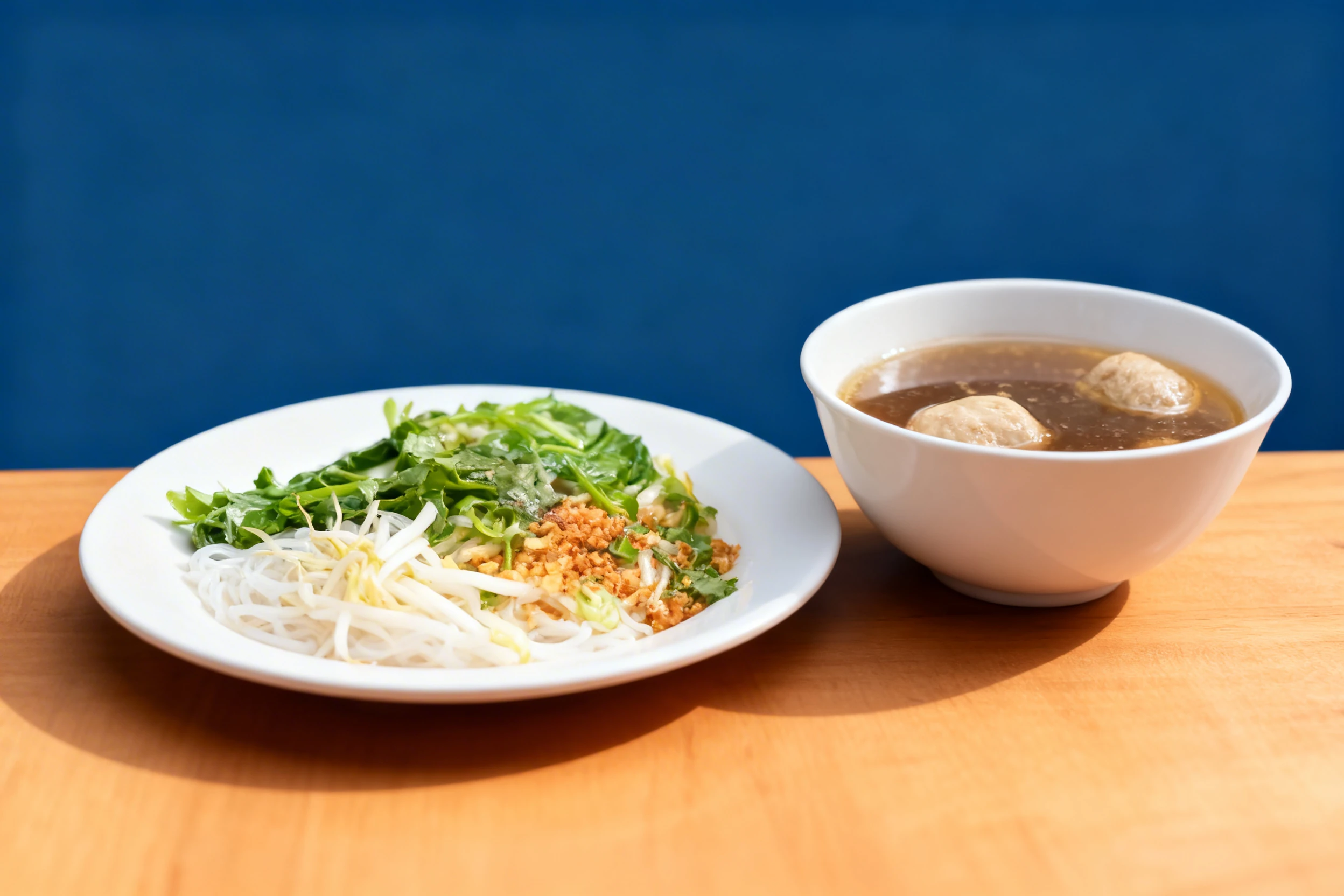 Rice noodle bowl with fresh greens, bean sprouts, and fried garlic, served alongside a plastic container of savory broth with meatballs.