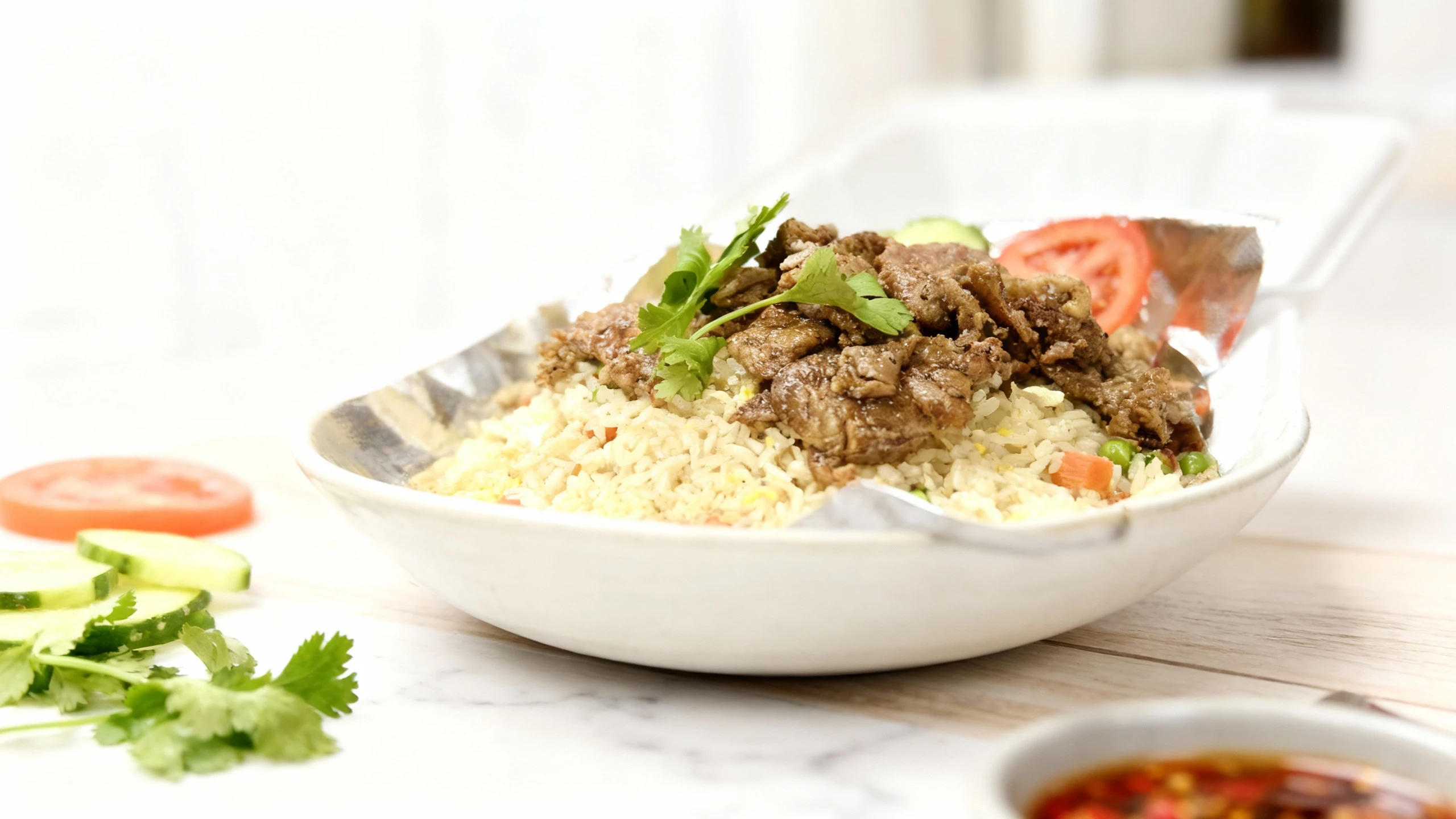 A large portion of fried rice mixed with diced carrots, peas, and egg, topped generously with savory slices of seared beef and garnished with fresh cilantro, ac