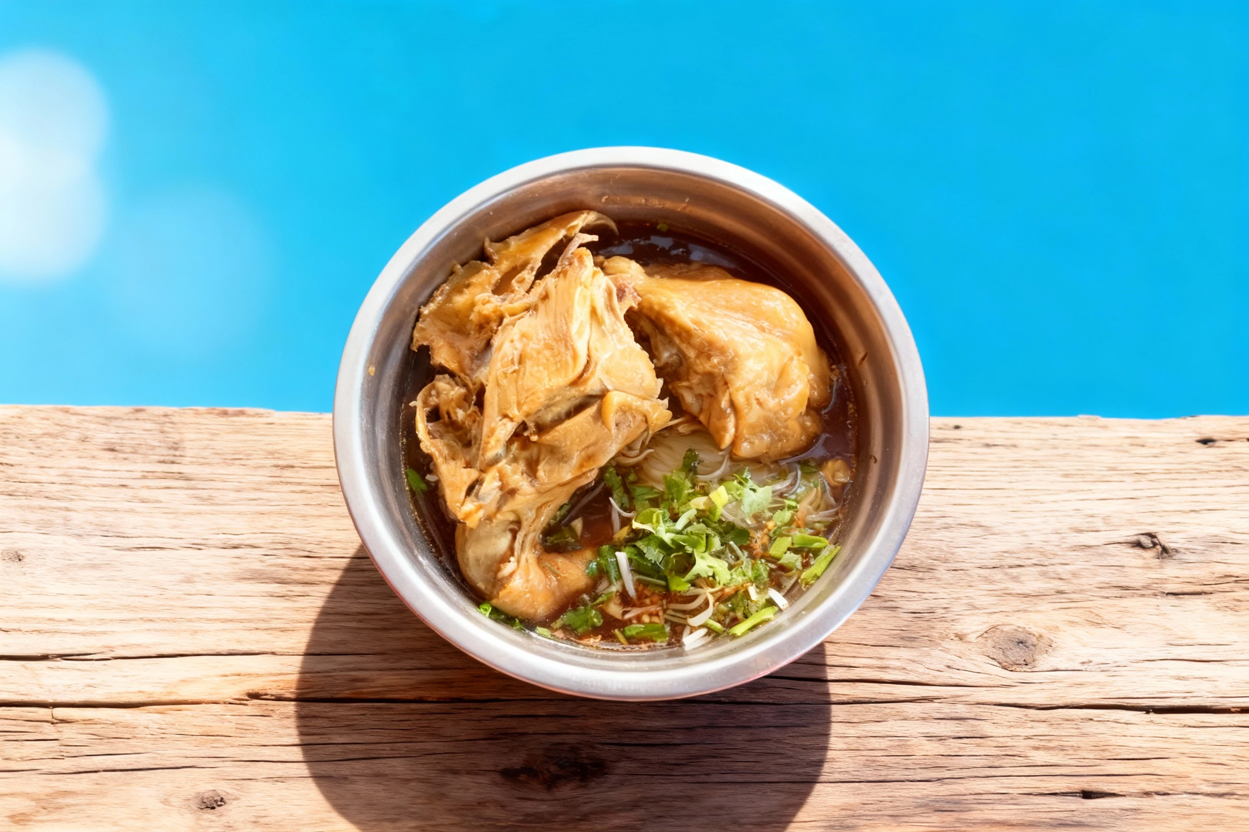 Chicken noodle soup featuring braised chicken pieces and thin rice noodles in a dark herbal broth, topped with chopped cilantro and spring onions.