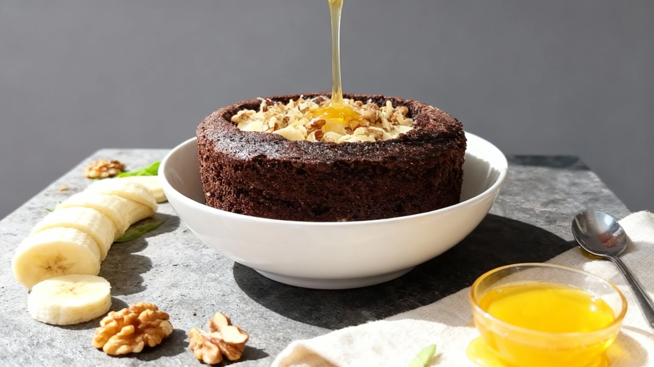 A deep, bowl-shaped chocolate cake or brownie base filled with cream, generously topped with overlapping slices of banana and chopped walnuts.