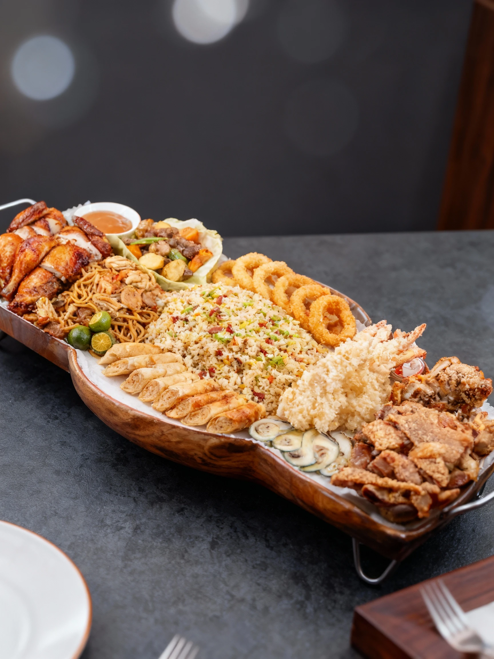 A massive Filipino-style feast platter featuring a central mound of shrimp and vegetable fried rice surrounded by roasted chicken pieces, crispy pork belly, bat