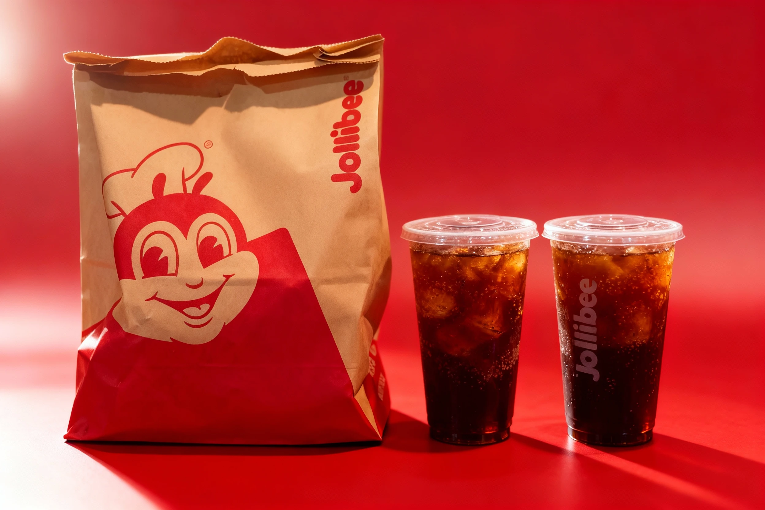 Jollibee takeaway order consisting of a large branded brown paper bag containing the main food items and two branded cold drink cups with plastic lids secured i