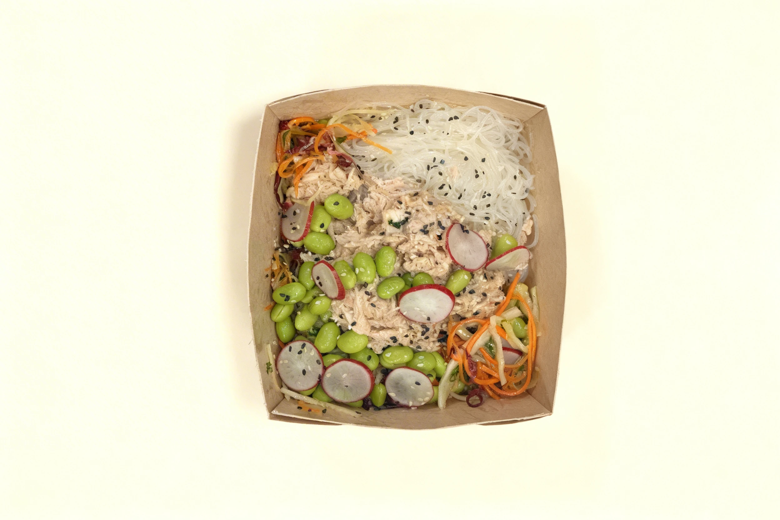 A chicken noodle salad featuring glass noodles, shredded chicken, edamame beans, sliced radishes, and julienned carrots topped with black and white sesame seeds