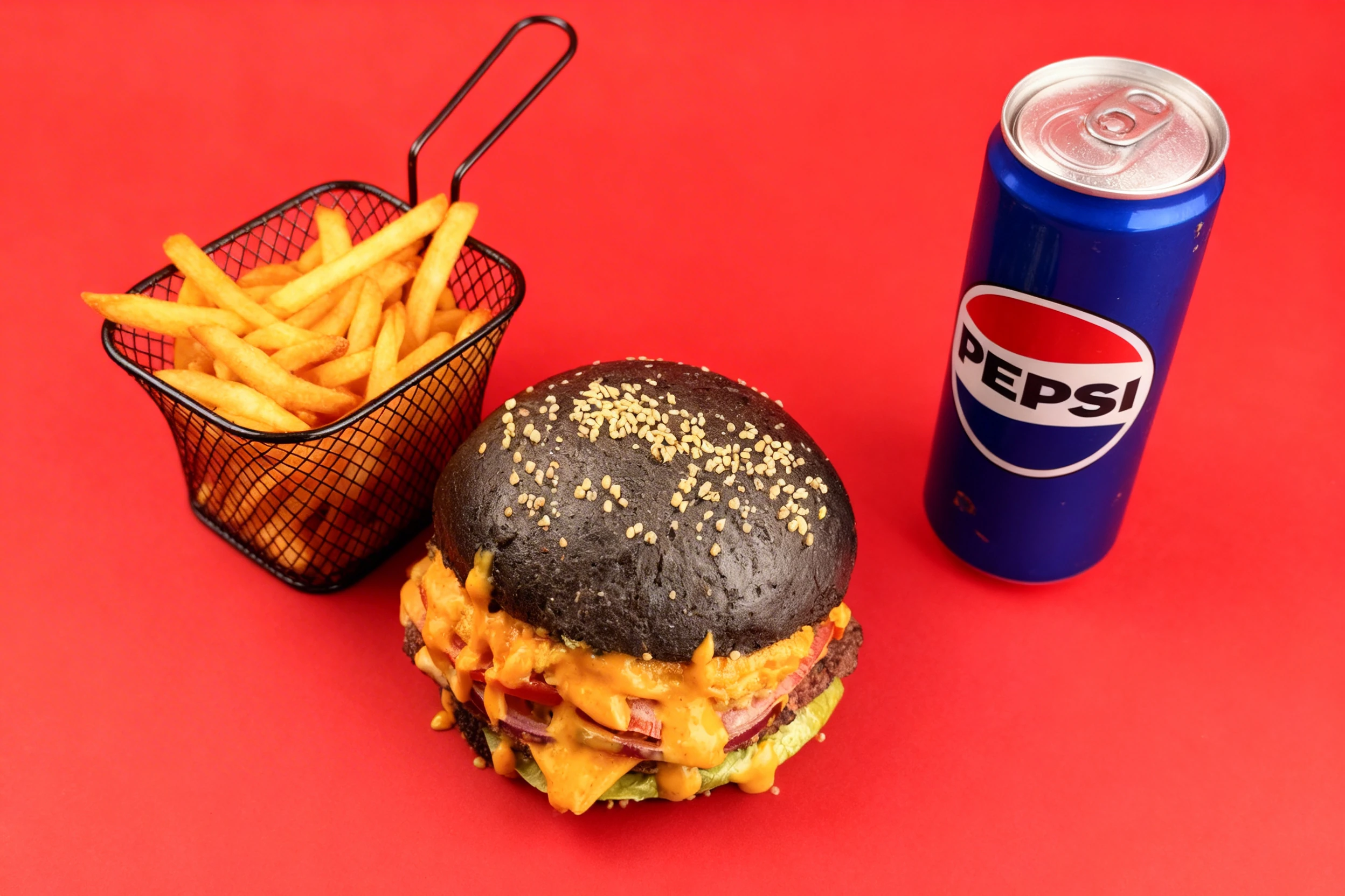 Double beef burger on a charcoal bun with melted cheese sauce, tomato, red onion, and lettuce, served with a side of french fries and a Pepsi can.