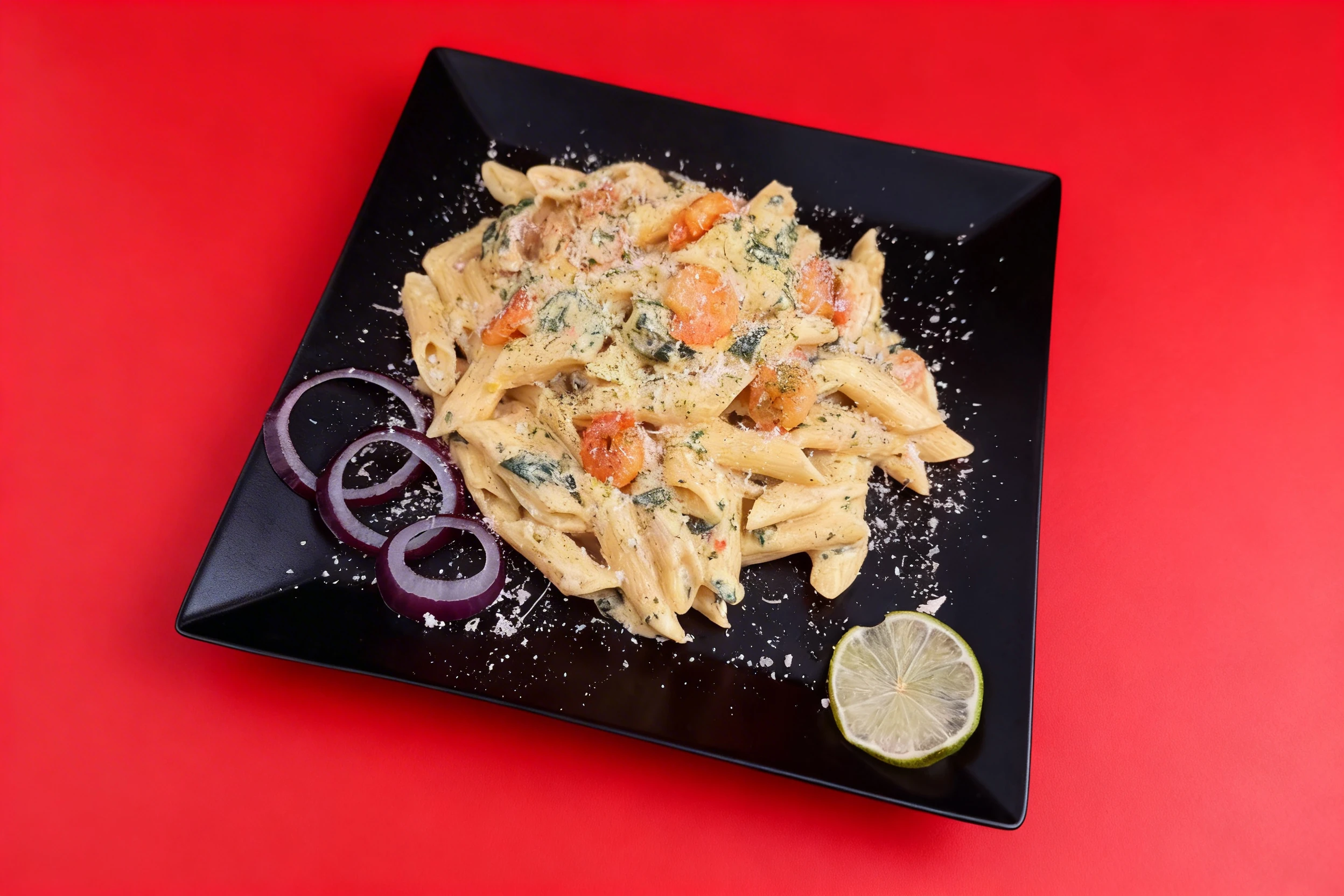 Shrimp and spinach penne pasta in a creamy sauce, garnished with grated parmesan cheese and served with raw red onion rings and a lime wedge.
