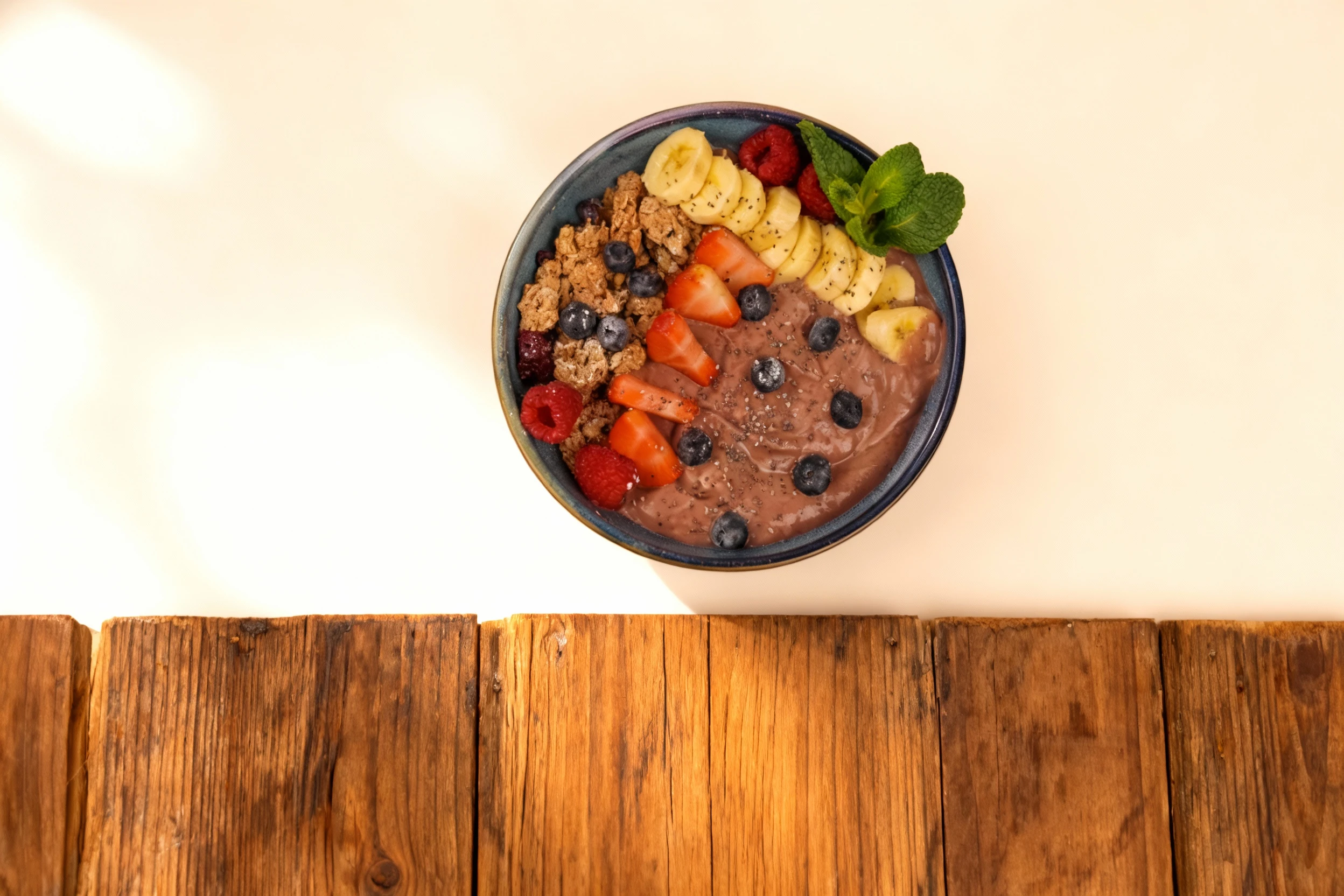 A berry smoothie bowl served in a blue ceramic bowl, topped with granola, sliced strawberries, raspberries, sliced banana, blueberries, and sprinkled with chia