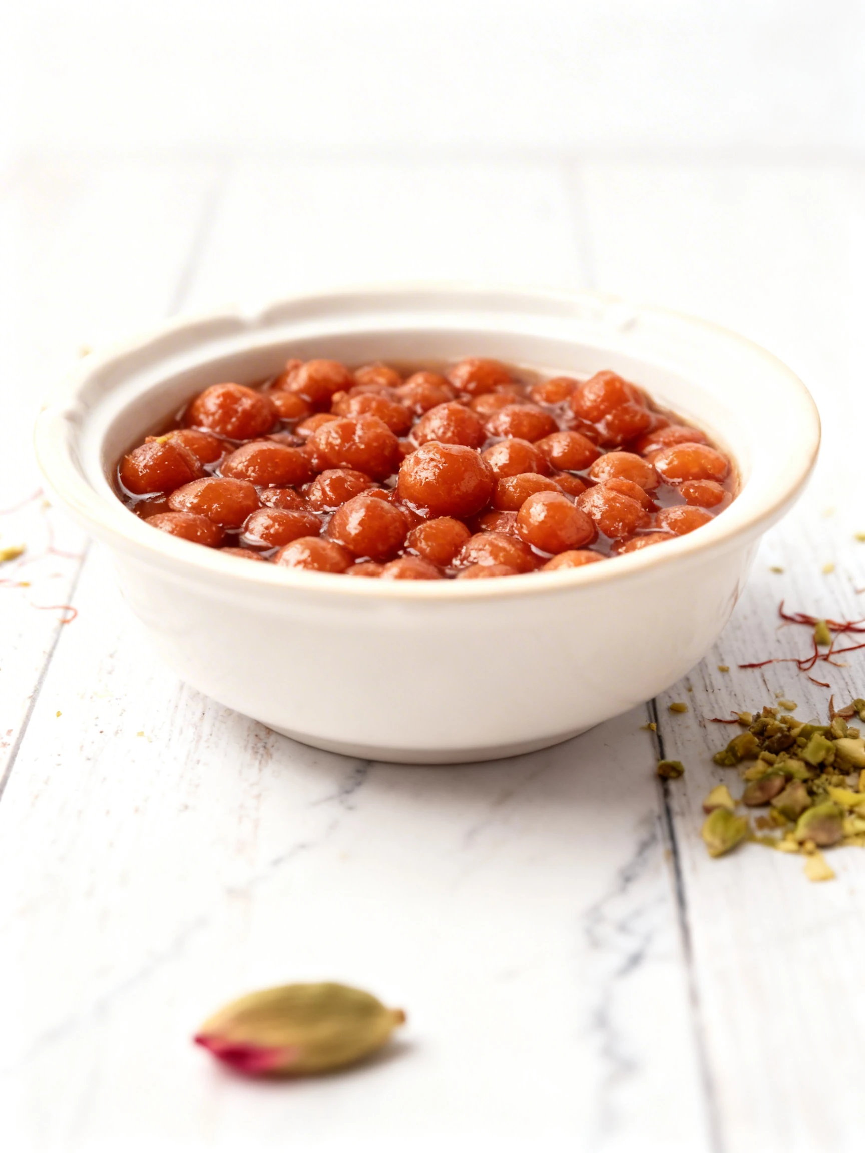 A close-up view of small fried dough balls, such as Gulab Jamun, soaking in a glossy sweet syrup within a container.