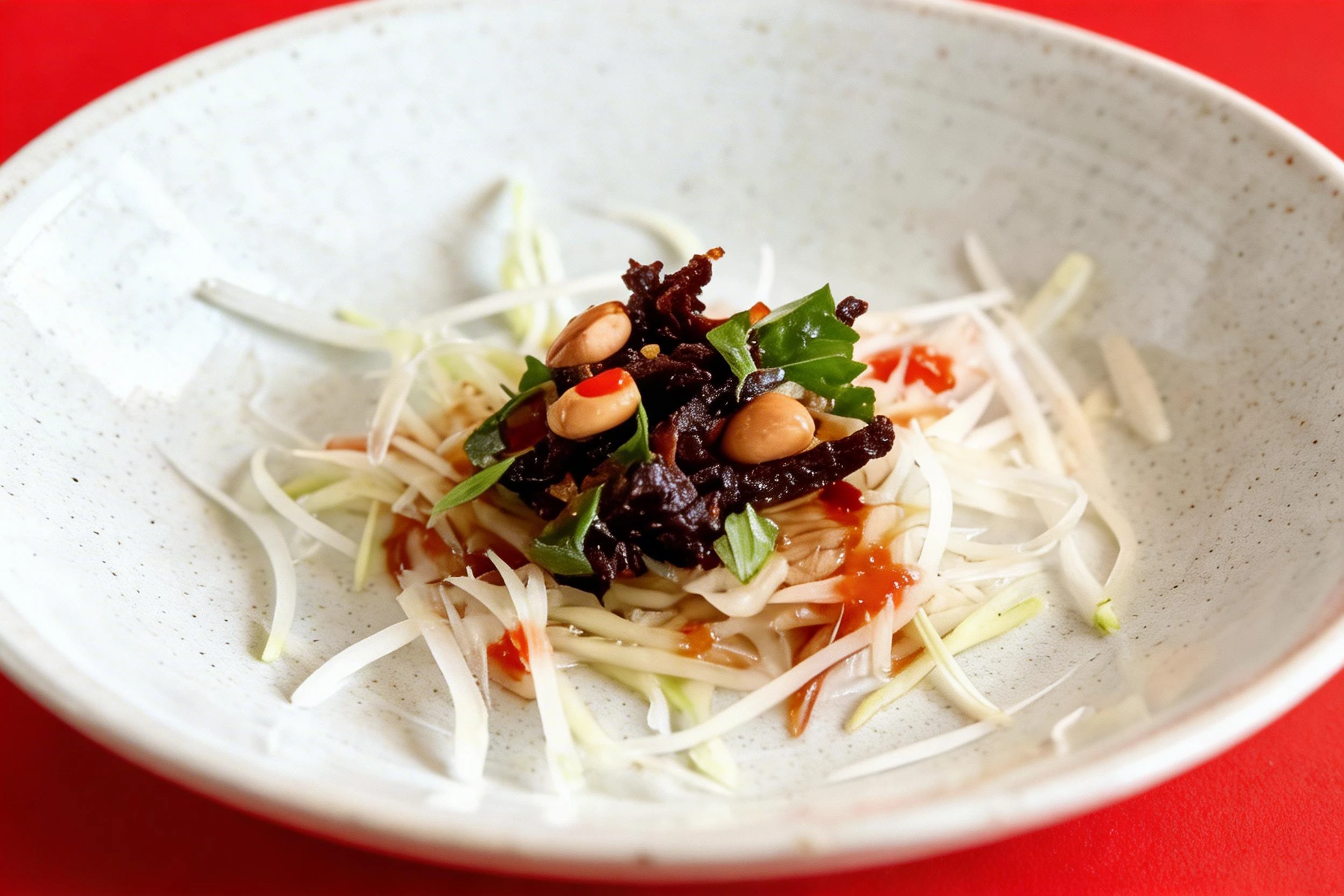 A small serving of green papaya salad topped with dark beef jerky, whole peanuts, fresh herbs, and chili sauce.