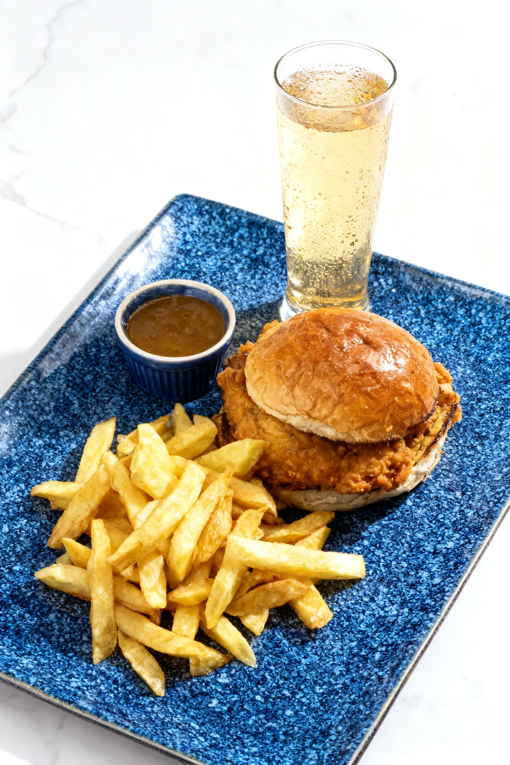 A fried chicken sandwich on a toasted brioche bun served with thick-cut fries, a plastic container of gravy, and a can of Coca-Cola.