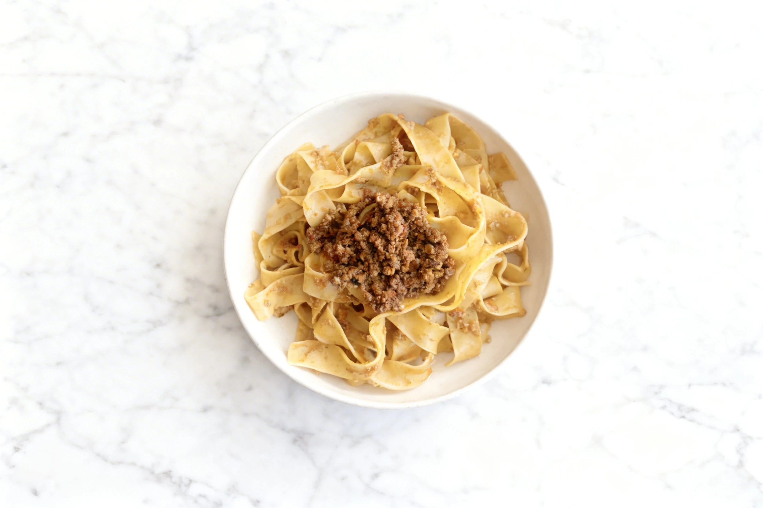 A bowl of wide pappardelle pasta tossed in a light sauce and topped with a generous portion of meat bolognese.