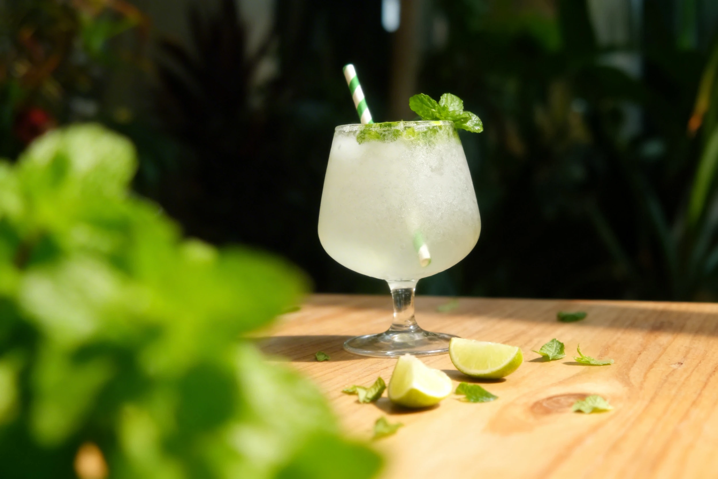 A lime mojito or citrus mocktail served over crushed ice with fresh mint leaves and a green-striped paper straw.