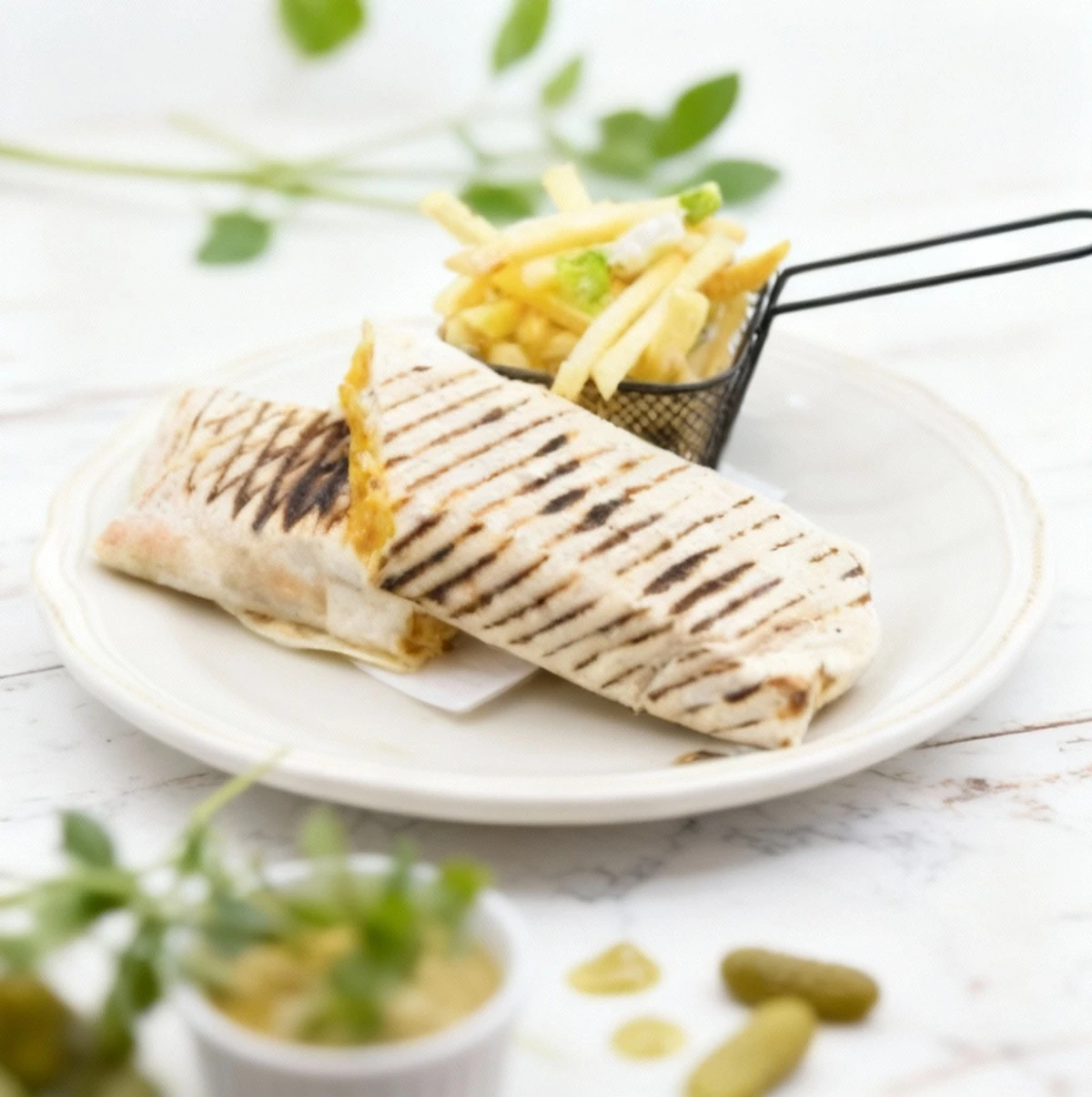 A tightly wrapped, pressed tortilla or panini, diagonally sliced and displaying dark grill marks, served with a side of French fries topped with white and green