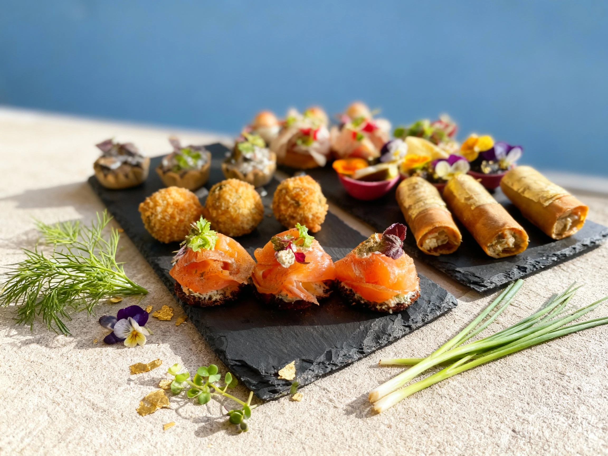 A curated assortment of gourmet canapés presented on black slate boards, featuring smoked salmon bites on dark bases, golden-brown croquettes, savory tartlets w