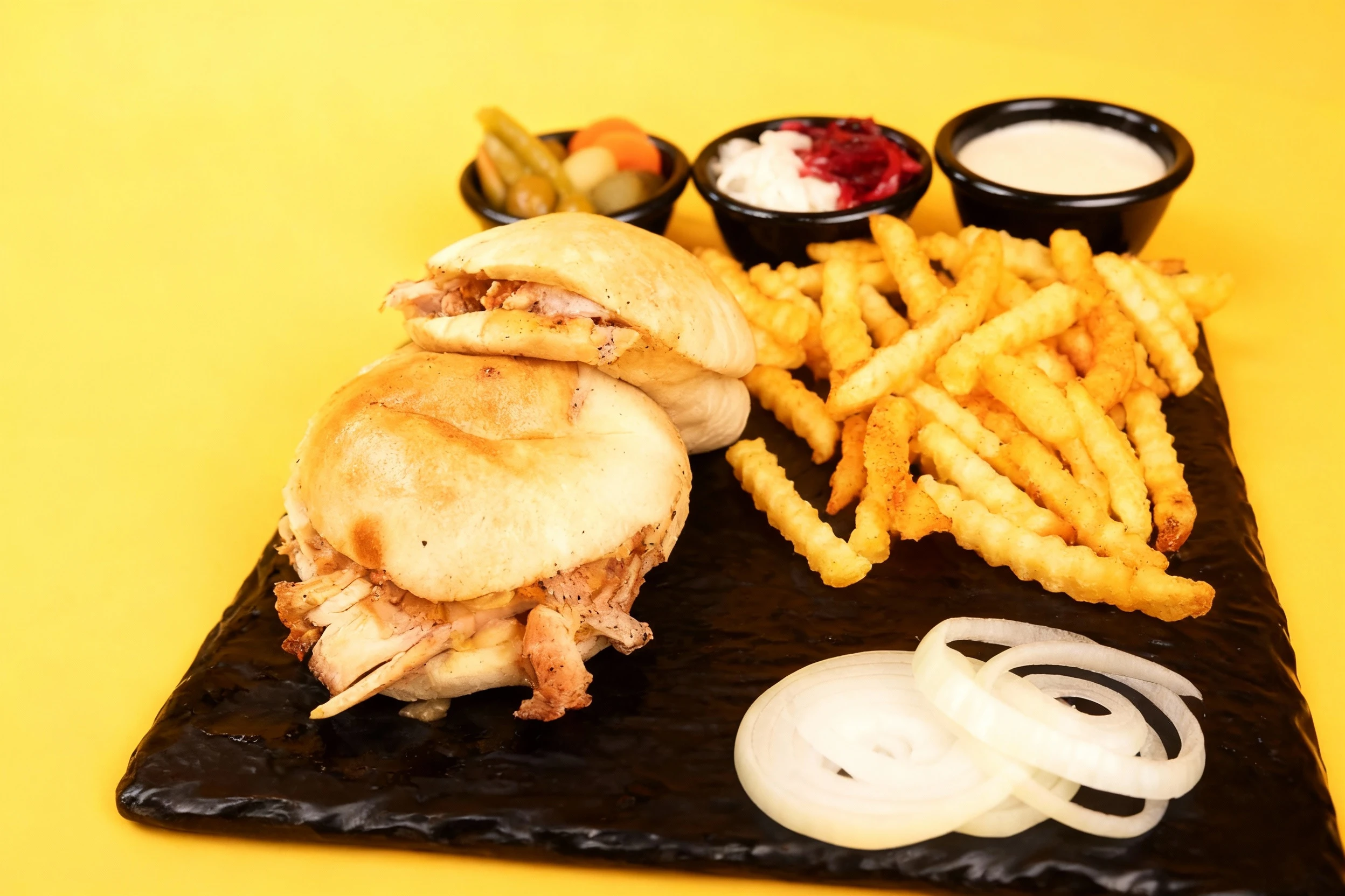 Chicken shawarma in pita bread served with seasoned crinkle-cut fries, tahini sauce, pickled vegetables, and sliced raw onions.