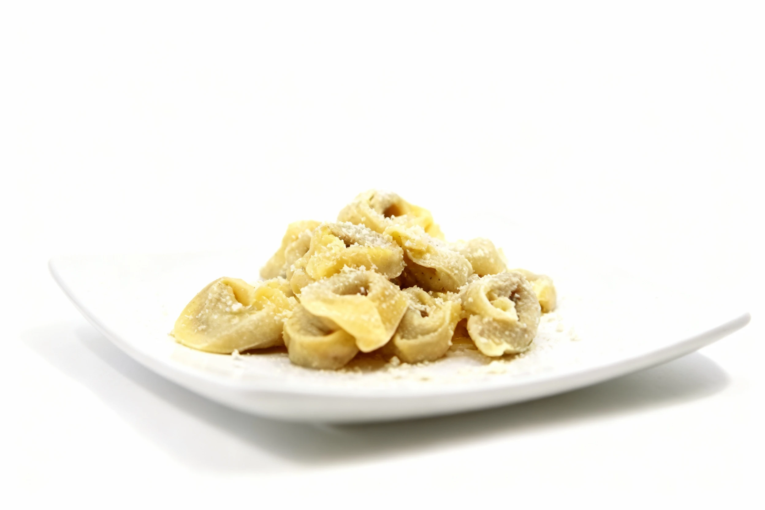 A portion of meat-filled tortellini pasta sprinkled with grated parmesan cheese and served on a white square plate.