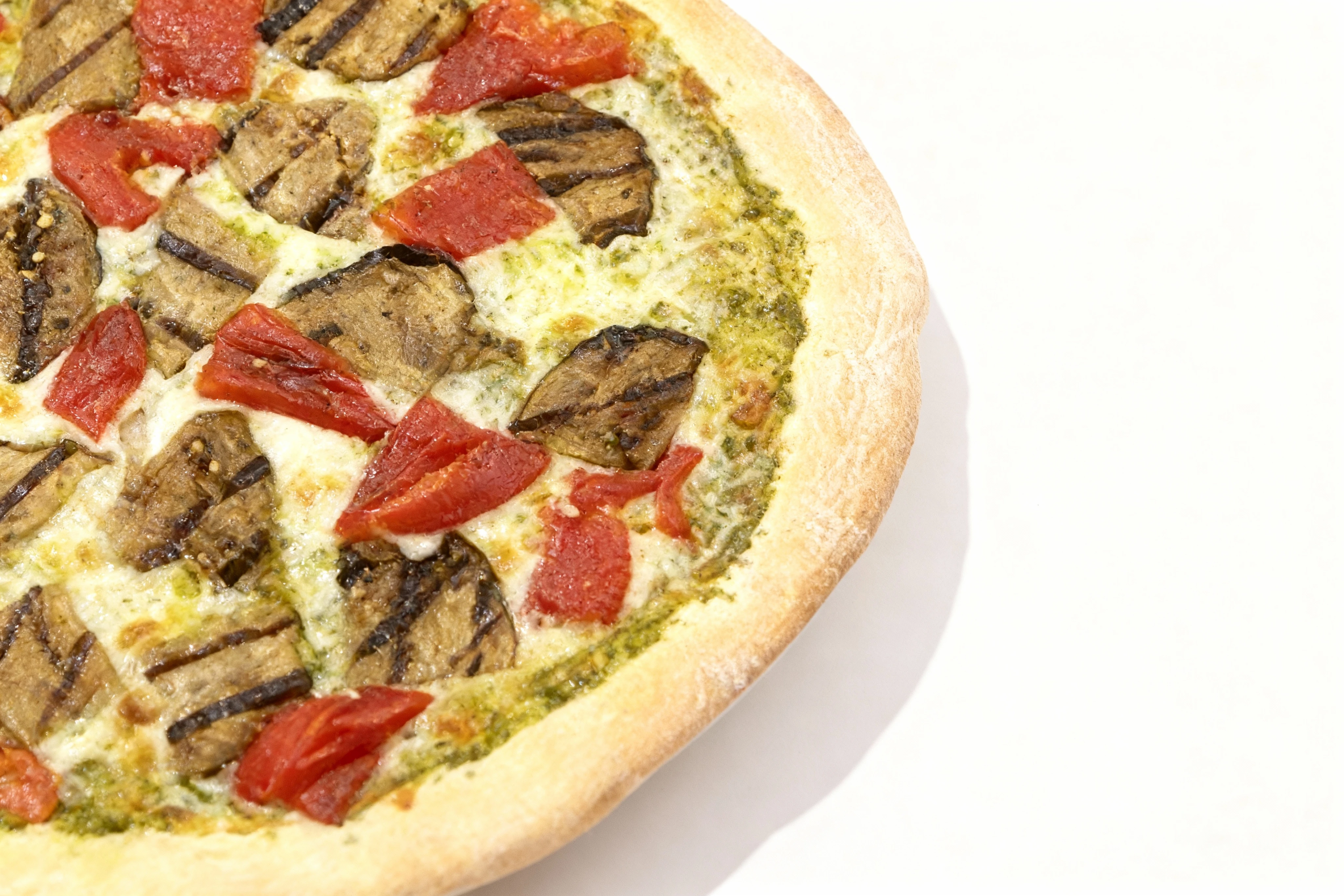 A vegetarian pizza topped with grilled eggplant slices, roasted red peppers, melted mozzarella cheese, and a pesto sauce base.